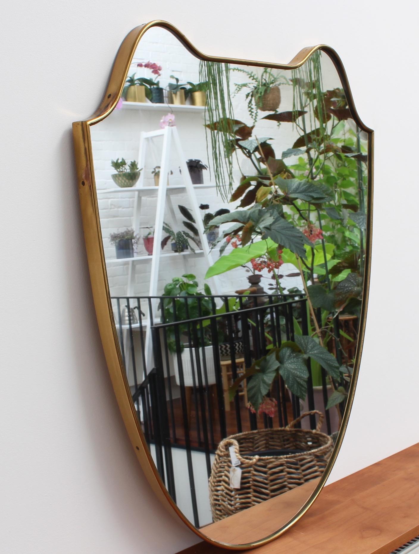 Midcentury Italian wall mirror with brass frame, circa 1950s. This mirror is substantial, solid and at once elegant. It is the movie star of vintage mirrors with its incredible looks, charming personality and characterful beauty marks that others