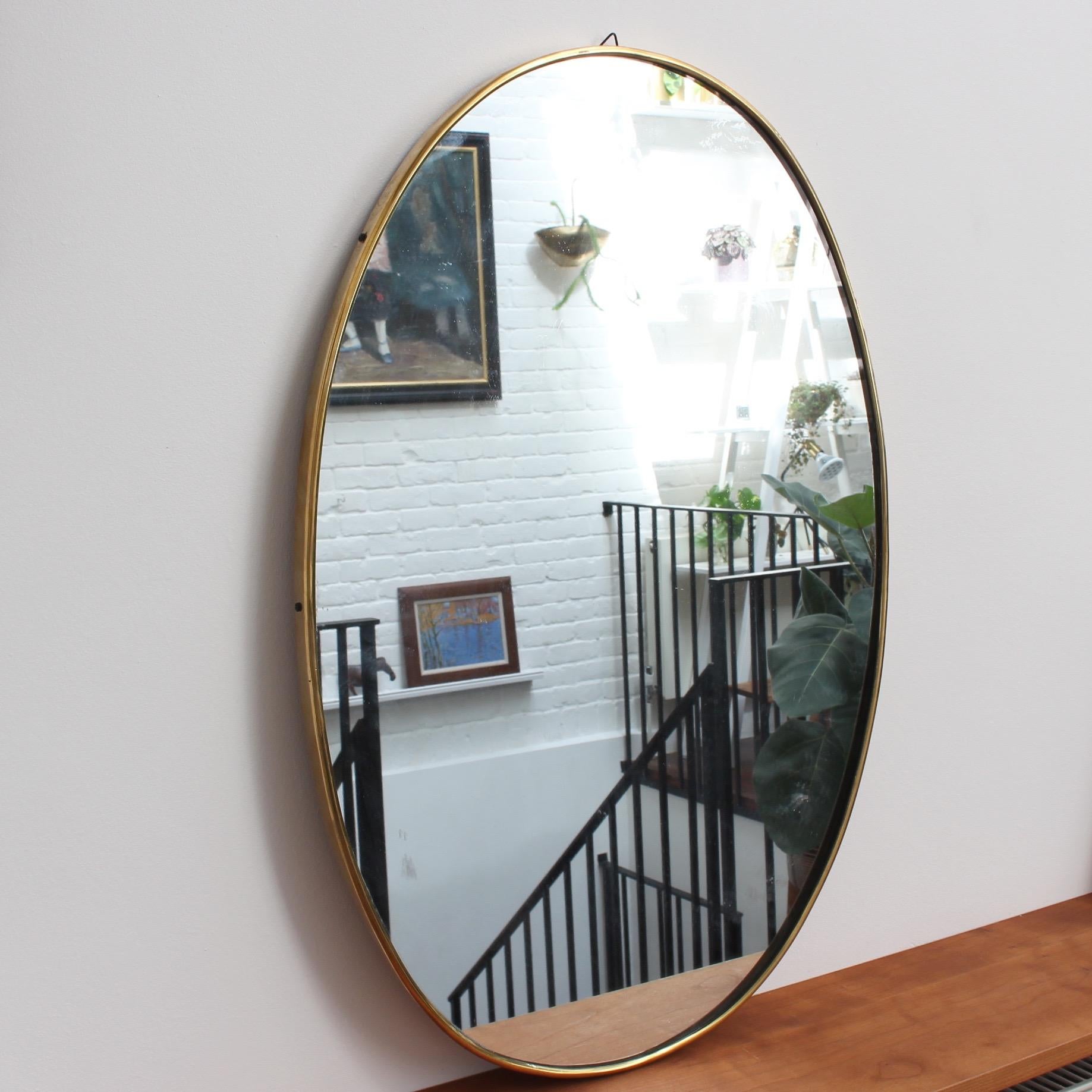 Midcentury Italian wall mirror with brass frame (circa 1950s). The mirror is beautifully oblong-shaped. Very elegant and distinctive in a modern Gio Ponti style. This mirror is in very good vintage condition. There are some characterful blemishes on