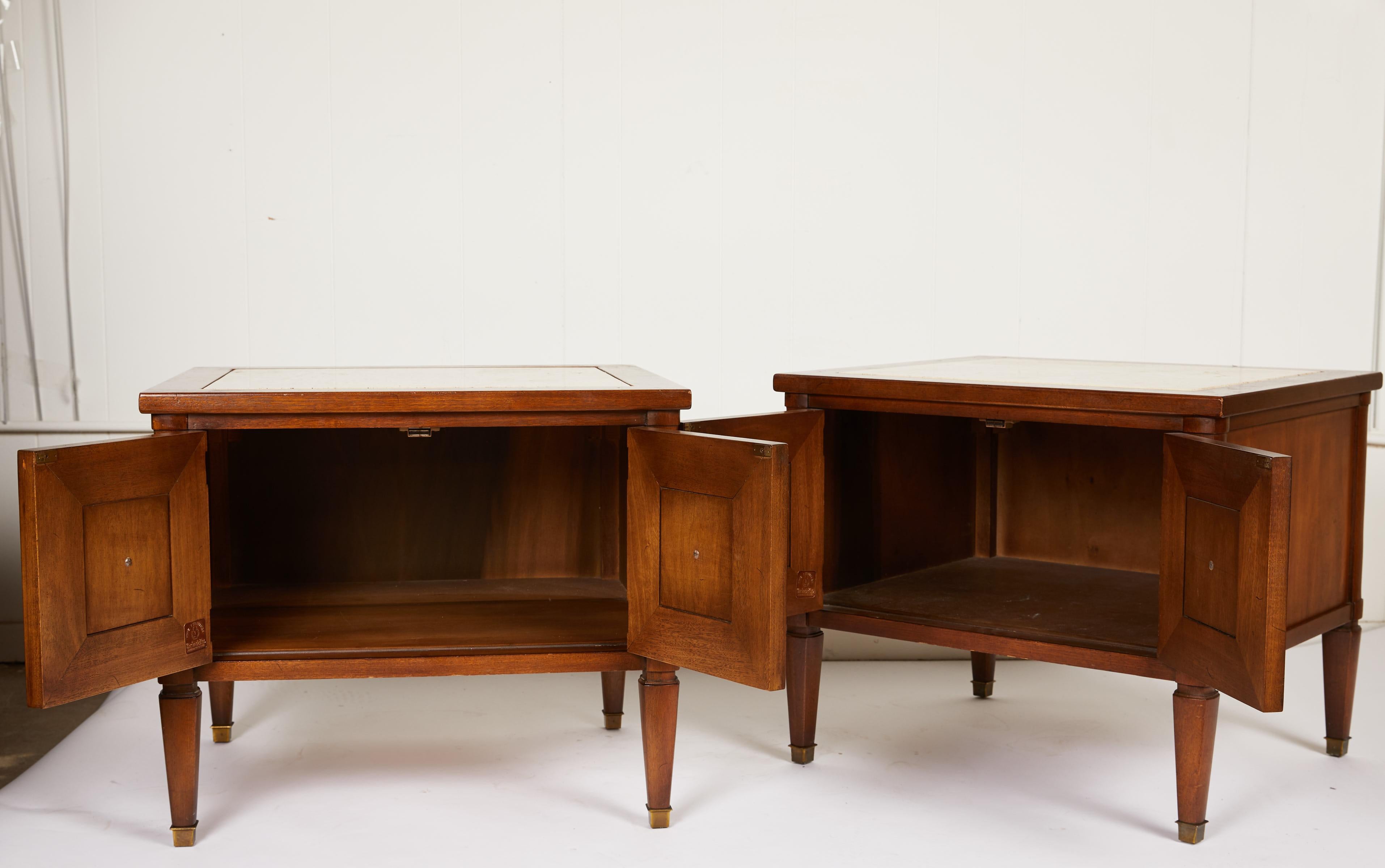 This Midcentury Italian pair of neoclassical style two-door end tables or bedside tables are made of walnut and finished on all sides. The tables are complimented by thick Italian travertine marble insets and bronze pulls and sabots. Marble marked