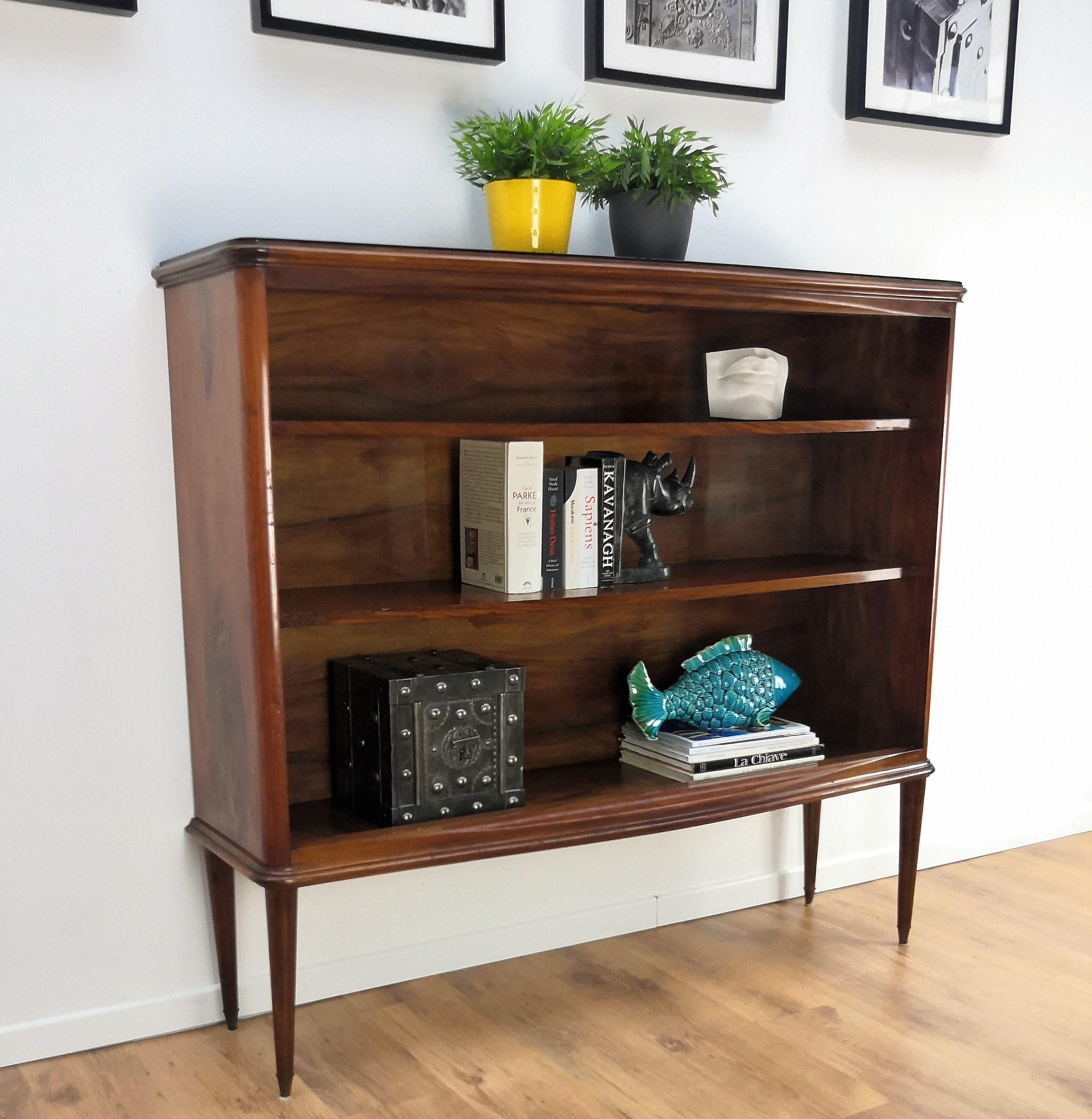 A beautiful Italian Walnut carved three shelves open bookcase, with great details and frames shaped in Victorian, Napoleon III, Louis XV style with Art Deco gilt decorated black glass top and Midcentury Modern accents such as the brass detail on the