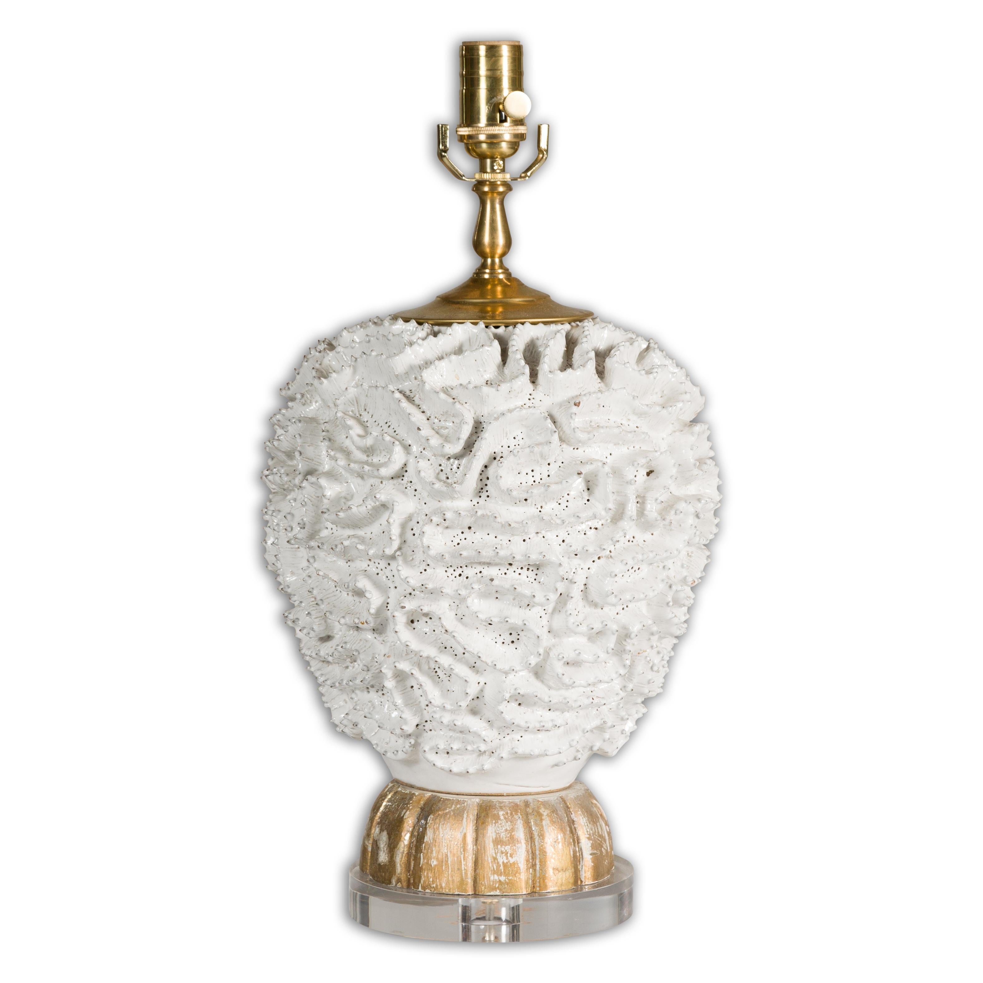 A Midcentury Italian white pottery table lamp with textured body and carved gilt wood base on round lucite. Emanating an aura of refined sophistication, this Italian Midcentury white pottery table lamp makes a powerful aesthetic statement.