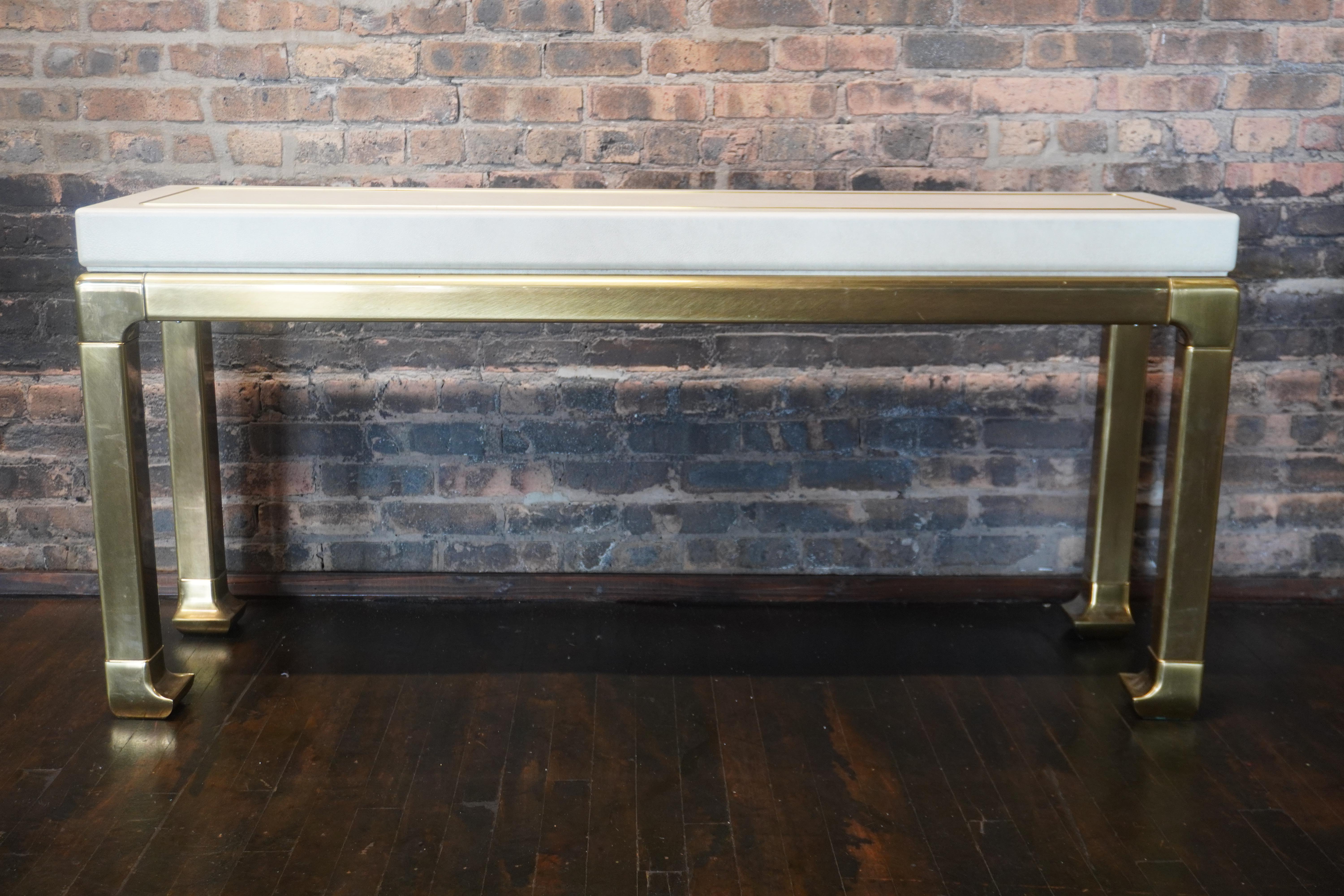 A lovely Mastercraft console table.  This table features a substantial brass base that is Chinoiserie in style.  There a cream colored leather wrapped (or quite possibly faux leather) top that has a thin line of brass inset all around the top of the