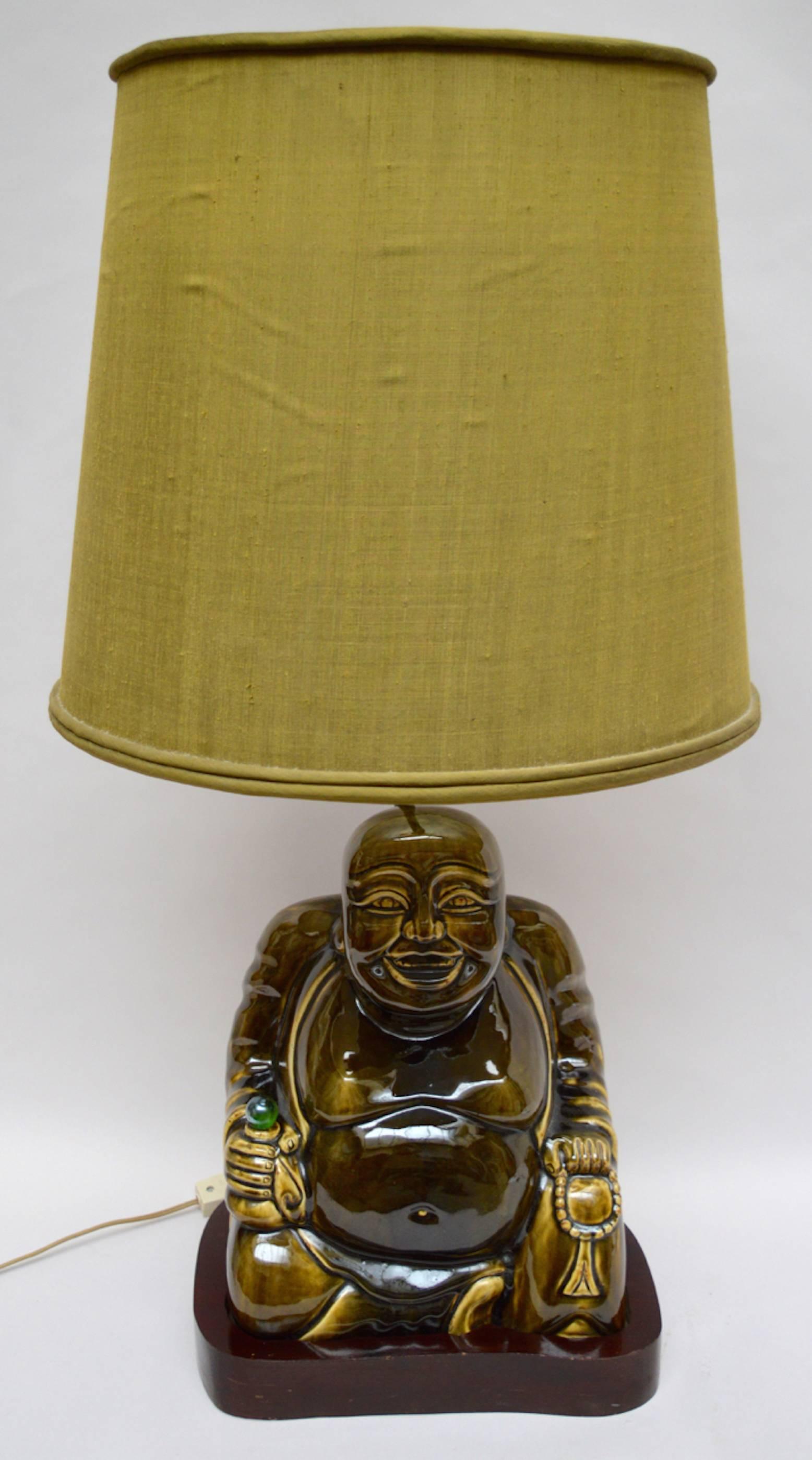 A large glazed porcelain Buddha mounted on a solid wood base retaining the original olive green raw silk lamp shade.
In the style of James Mont who was known as the bad boy of decorating.
Mont, who was born in Constantinople, claimed; I am an