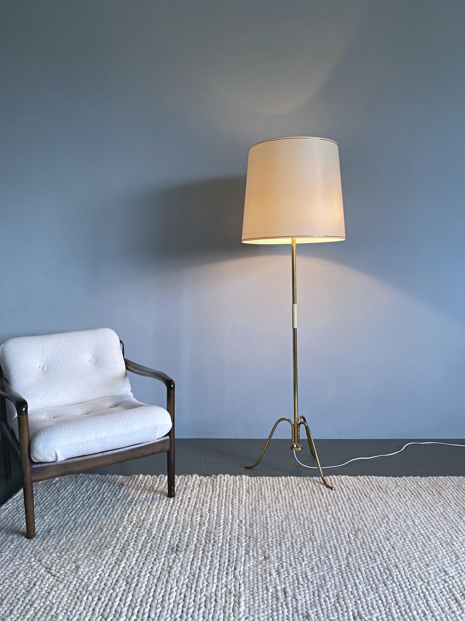 Lampadaire simple et élégant de style midcentury par J.T. Kalmar fabriqué à Vienne dans les années 50. La lampe est composée d'un tube en laiton et d'une base tripode en laiton poli. Le grand abat-jour permet d'obtenir une lumière douce sur une