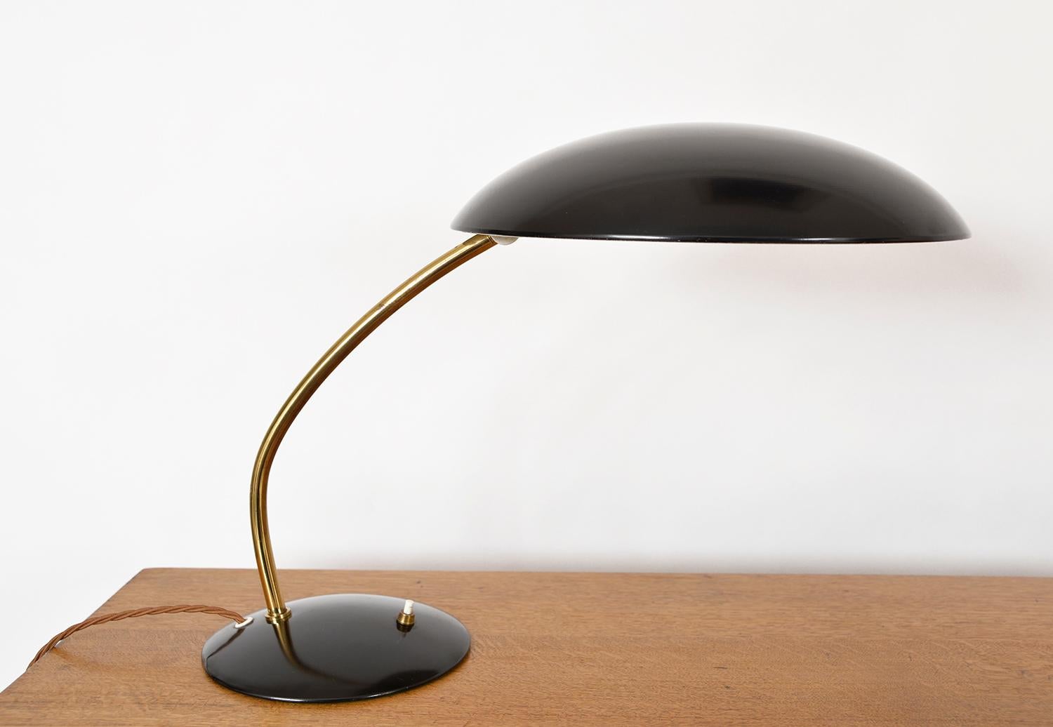 Original 1950s black enameled Kaiser Idell desk lamp by Christian Dell, model ‘6782’ with a curved pivoting brass arm and ball joint mechanism, which allows the shade to be rotated and tilted.
This timeless desk lamp, sat on green baize, is in very