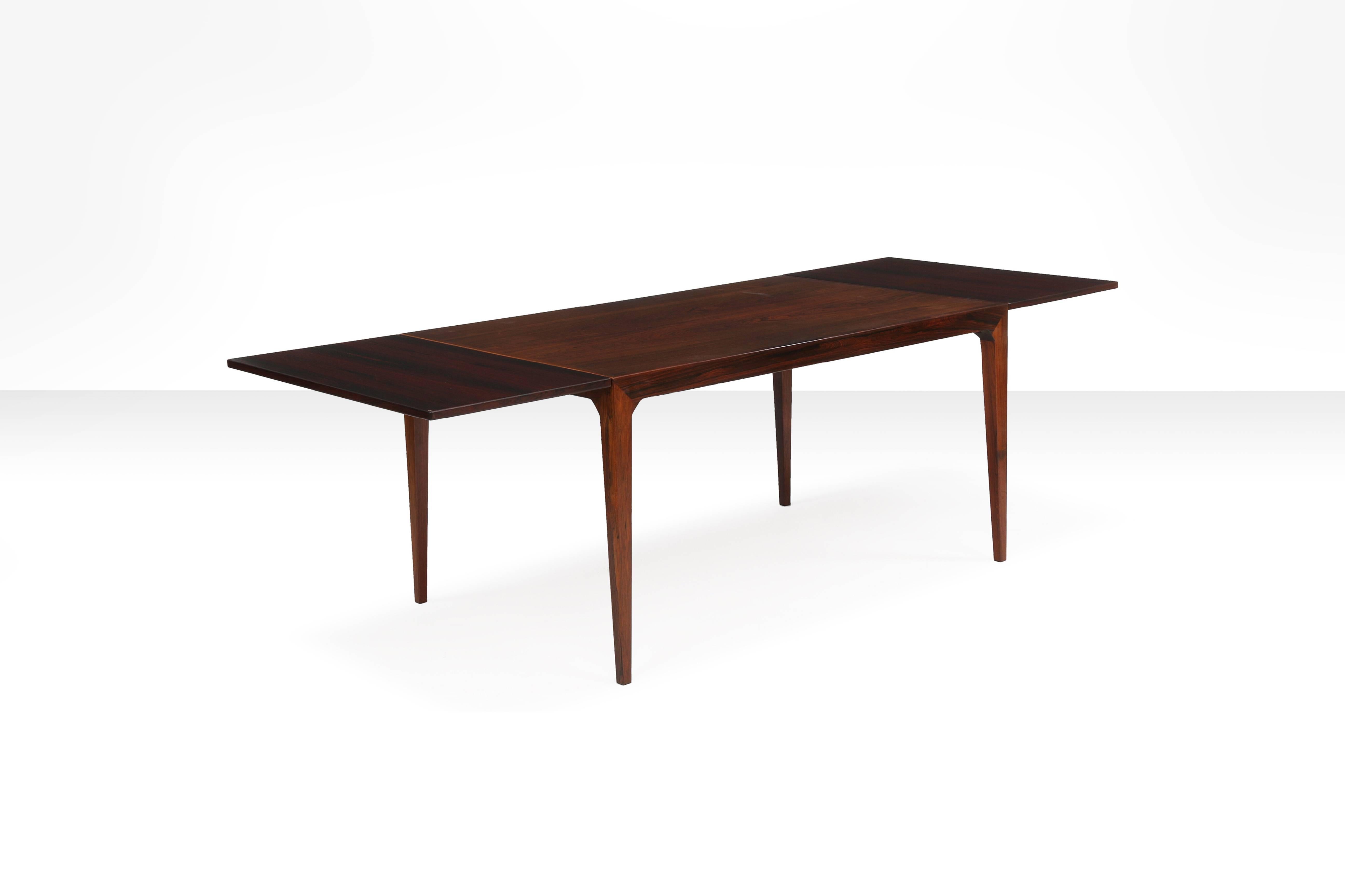 Rectangular rosewood dining table with two extra leaves, rail with carved handles for pulling out support beams for extra leaves. Mounted on tapering legs. 

Measurements:
140 (/189 cm with extra leaves) L x 90 cm W x 74 cm H.

This dining
