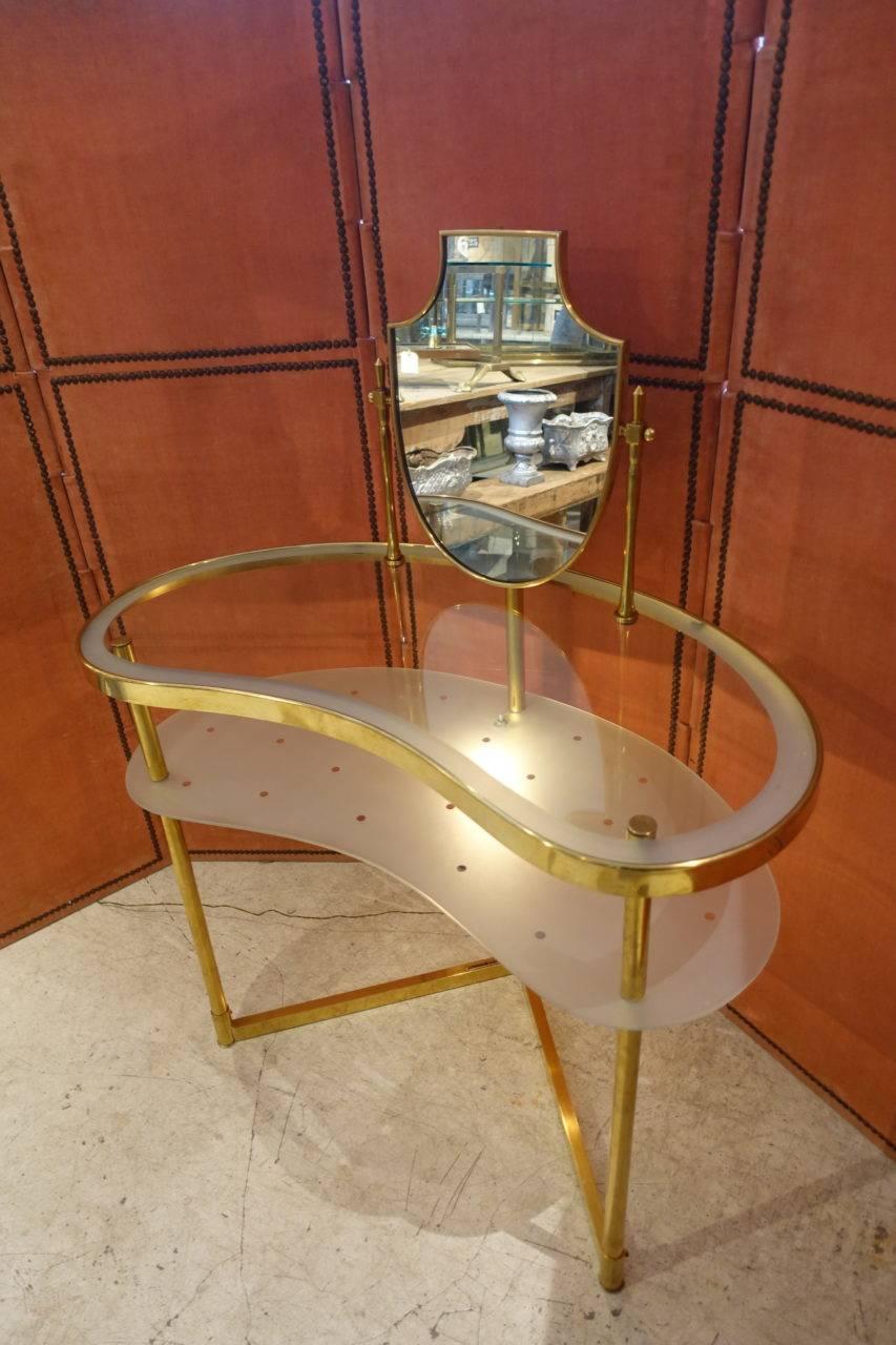 An absolutely charming midcentury French kidney shaped side or dressing table, made of brass and glass. This 1950s piece has a tabletop with an elegantly in built and tilting mirror. Underwhich there’s a matte glass shelf, delicately patterned with
