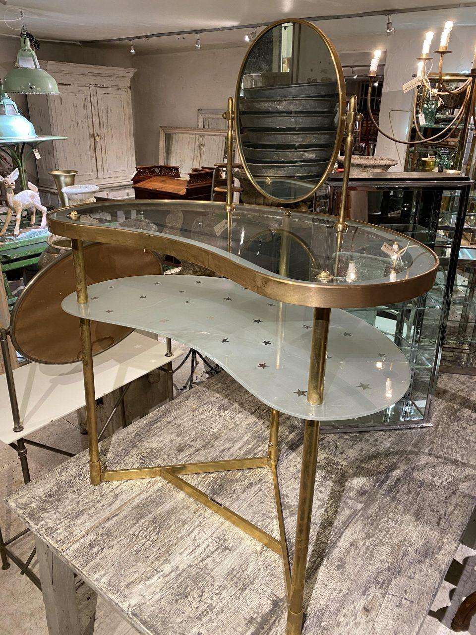 Stylish midcentury French vanity table and mirror. Beautiful kidney shaped form, with a beautifully slender and elegant brass frame and two glass shelves, one being opaque and the other charmingly decorated with small stars. The oval tilting mirror