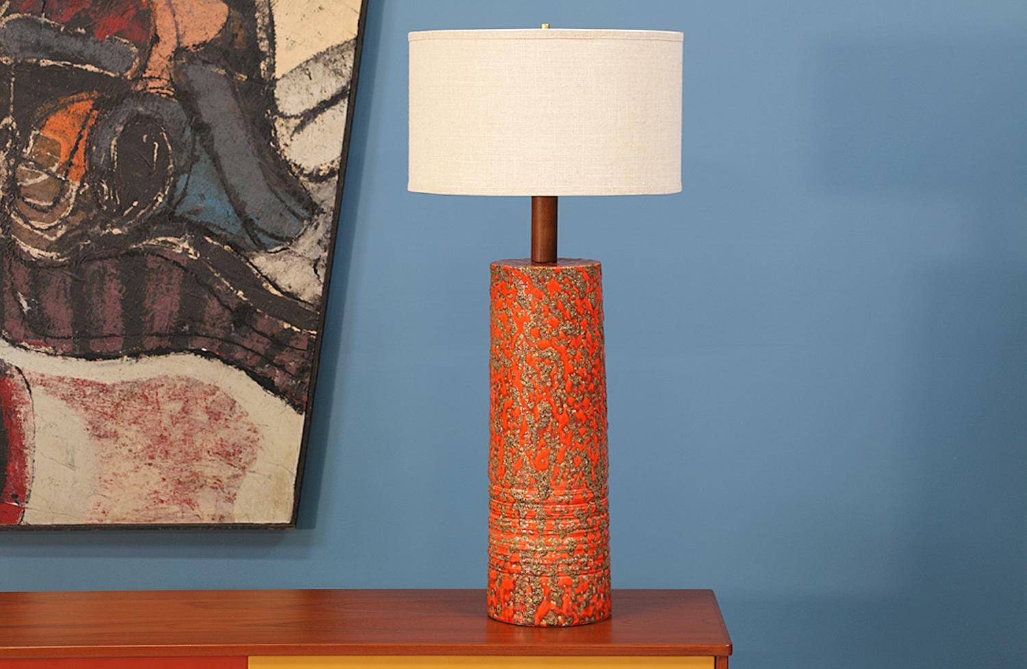 Mid Century Modern ceramic table lamp designed and manufactured in the United States circa 1950’s. Its cylindric body has a dripped lava-glazed texture in orange and brown hues that is complimented by the walnut wood neck. Includes custom linen