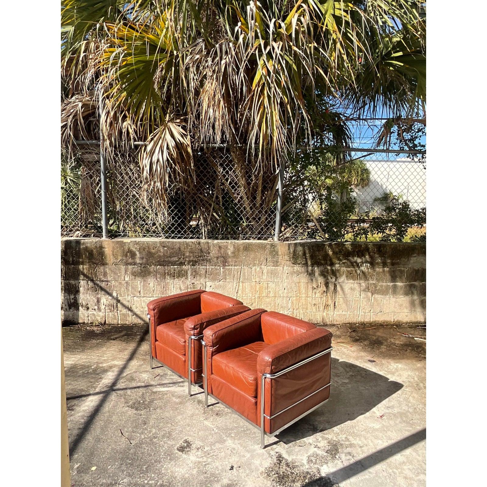 Fantastic vintage pair of Midcentury arm chairs. Done in the manner of the LC2 arm chair for Corbusier. Beautiful warm caramel colored leather with the most perfect distressed finish. Iconic chrome frame. Acquired from a Palm Beach estate.