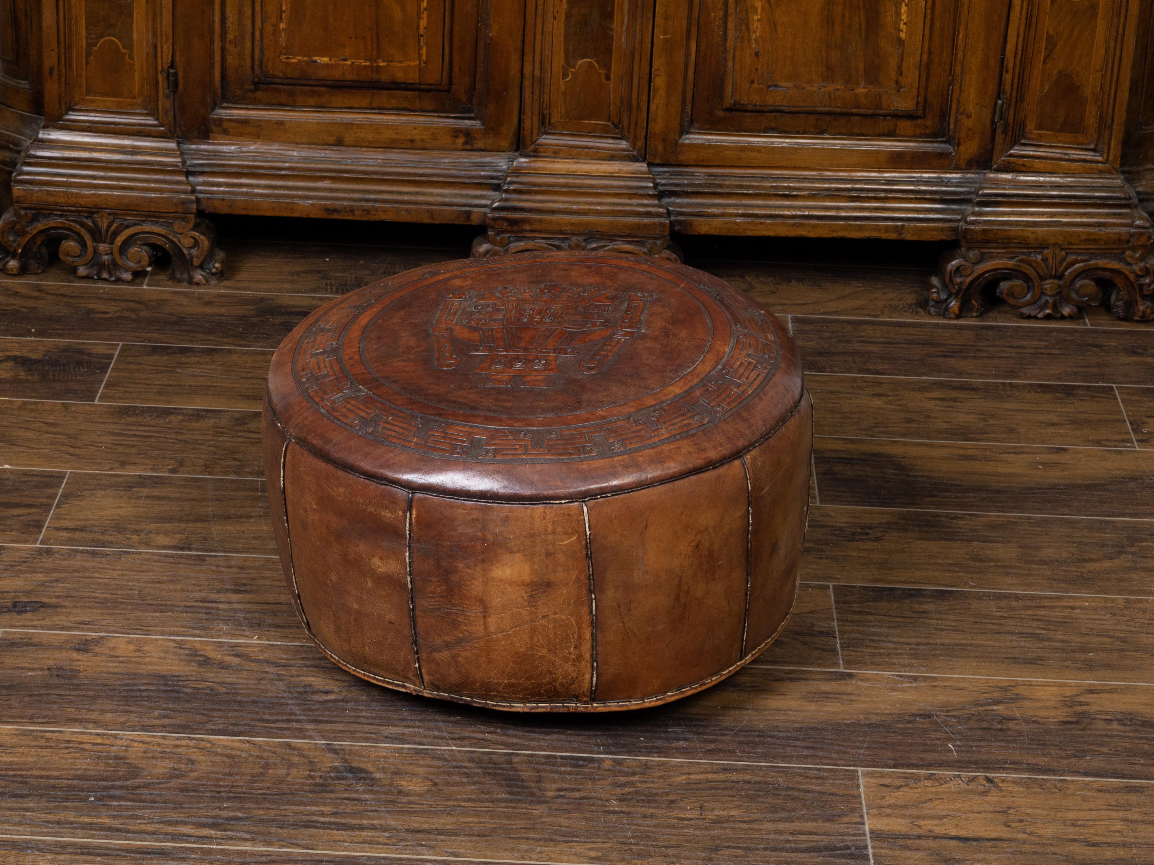 A vintage leather pouf from the mid 20th century, with Mesoamerican motifs and dark brown patina. Created during the midcentury period, this leather pouf captures our attention with its central Mesoamerican tooled décor surrounded by a meander