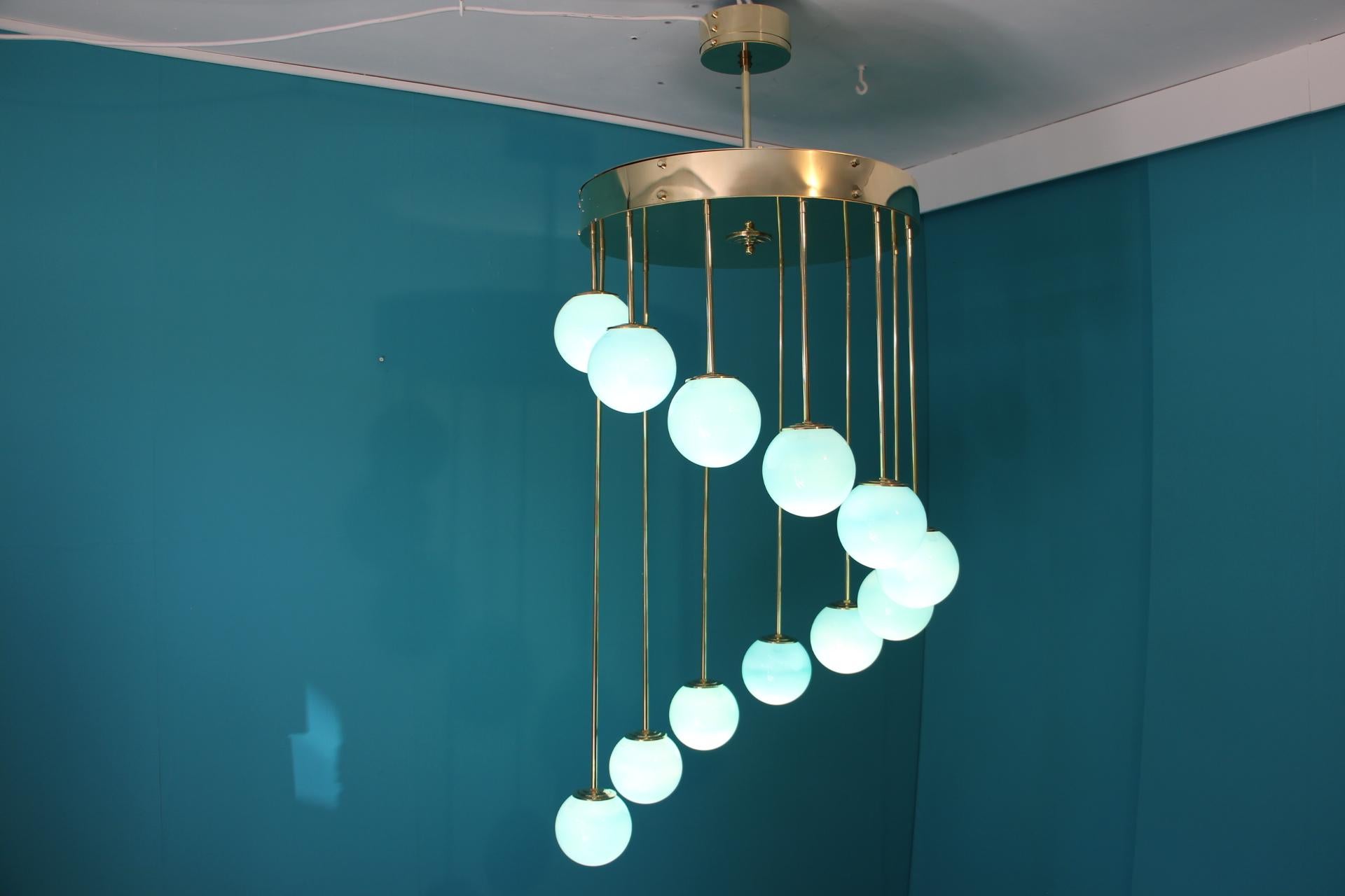 This spectacular chandelier features a main brass disk top from which fall 12 brass rods of different length in a spiral shape.
 Each rod is ending with a Murano glass globe.
Each globe was handmade in a magnificent Tiffany blue color.
It gives a