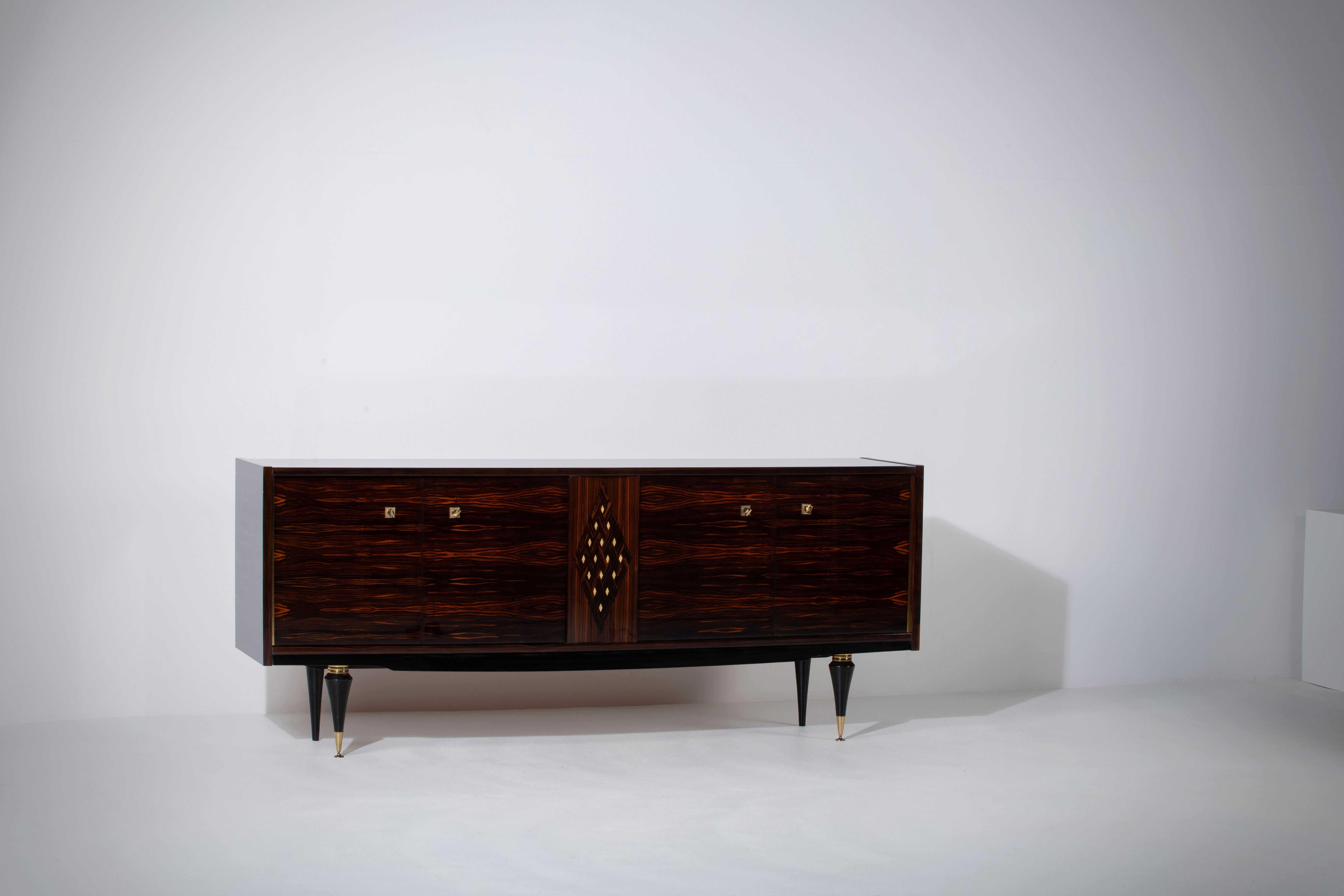 French Art Deco sideboard, credenza, with bar cabinet. 
The sideboard features stunning Macassar wood grain and rich pattern, mother of pearl. It offers ample storage, with shelves.
The case rests on tall tapered legs with brass details. 
A