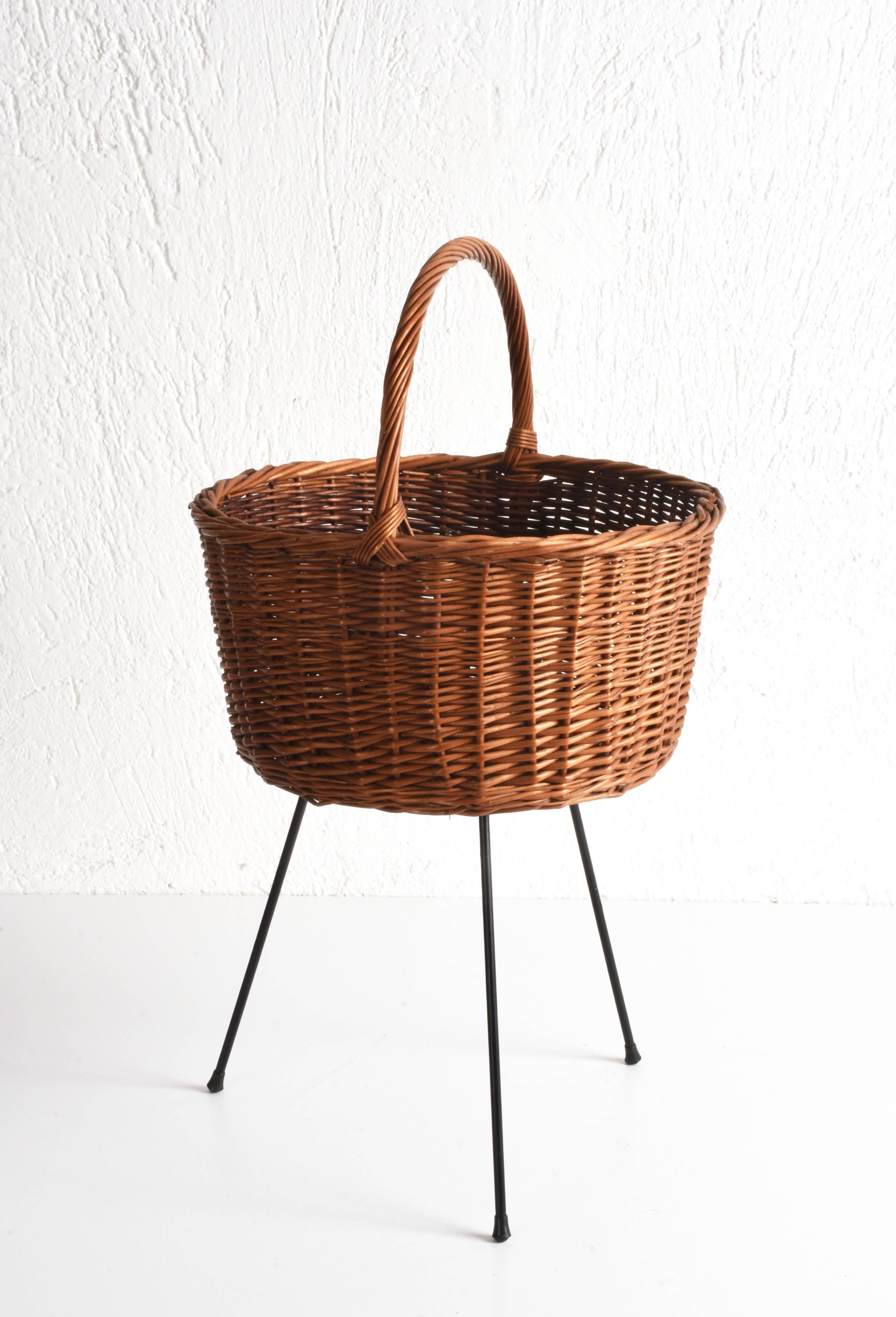 Midcentury Italian-made wicker basket produced in the 1950s. 

It can be used as a magazine rack and it has the base in black painted metal with feet and the basket has a woven wicker handle. 

Very good general conditions with some signs due to