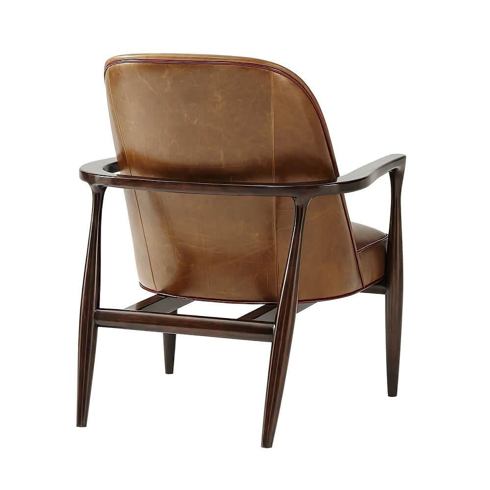 A Mid-Century Modern style leather upholstered barrel back mahogany armchair. An elegant streamlined example of popular midcentury furniture design.

Upholstered in Portland leather
Trim: Contrast Welting in Avignon Leather.