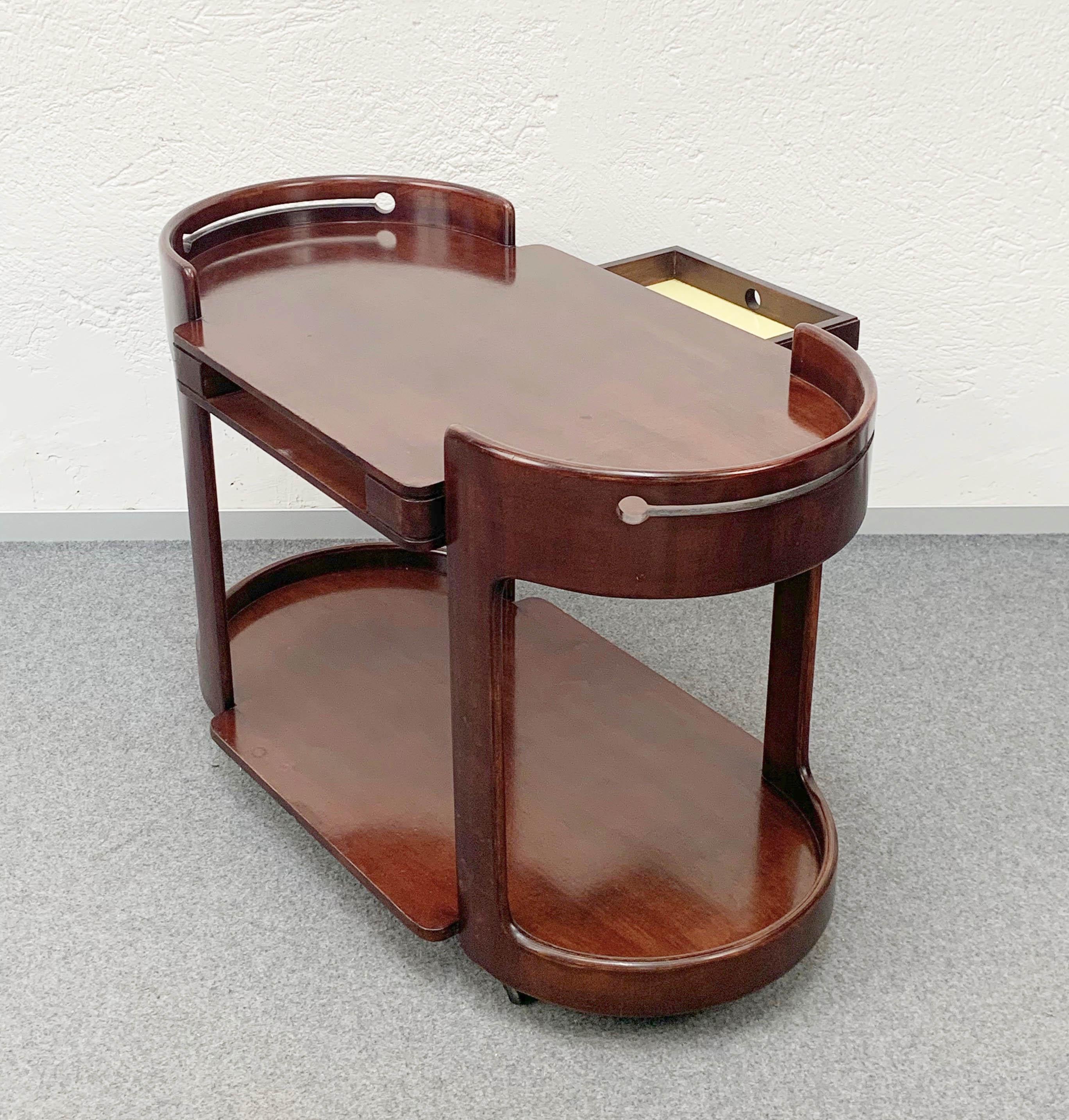 Elegant midcentury bar trolley after Afra and Tobia Scarpa in mahogany wood. The item was produced during 1970s in Italy and it is in marvellous conditions. 

It has a sliding drawer that can be opened from both sides and can be used as a tray.