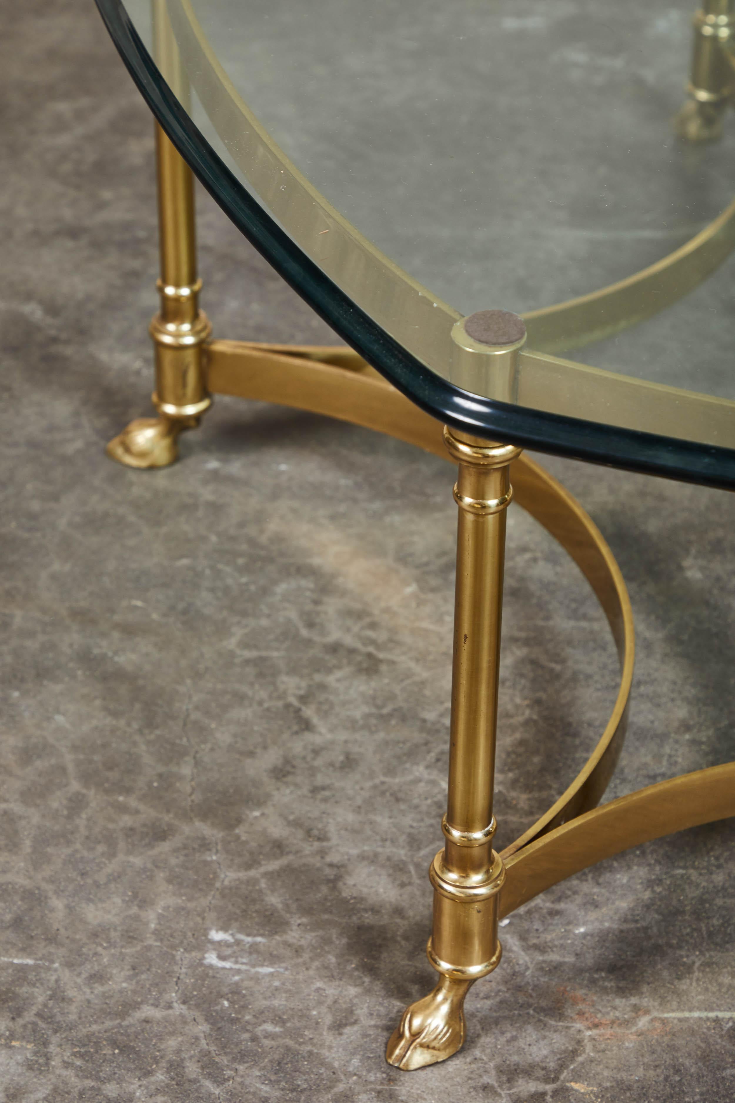 Maison Jansen style mid-20th century six legged coffee table in brass and glass. The brass legs of this coffee table are cleverly carved to resemble the hooves of an animal. The stretchers curve deeply inward and back between each pair of legs.