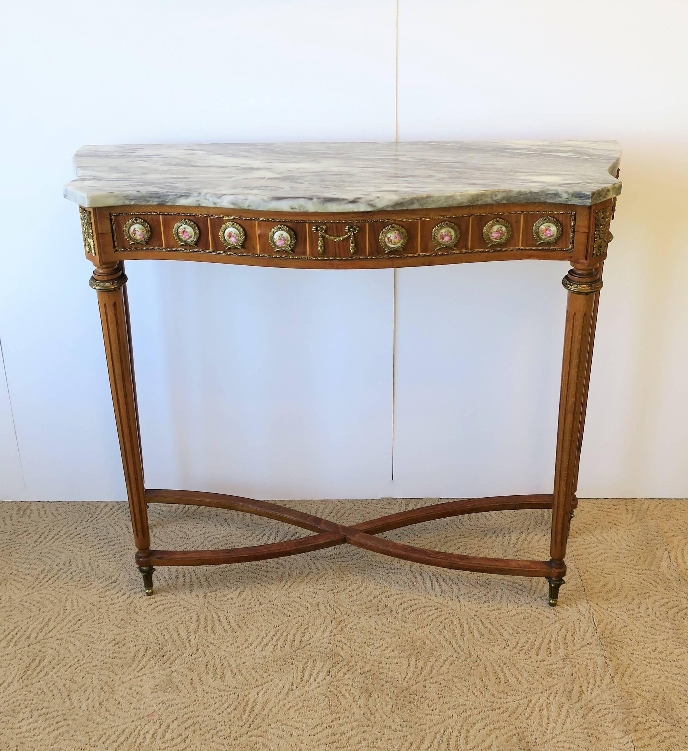 A console table with grey/dark grey/white marble top, wood base, and porcelain and brass ormolu mounts, in the Regency style, circa mid-20th century, 1960s. Details include substantial marble top, shape of marble top, brass and porcelain mounts with