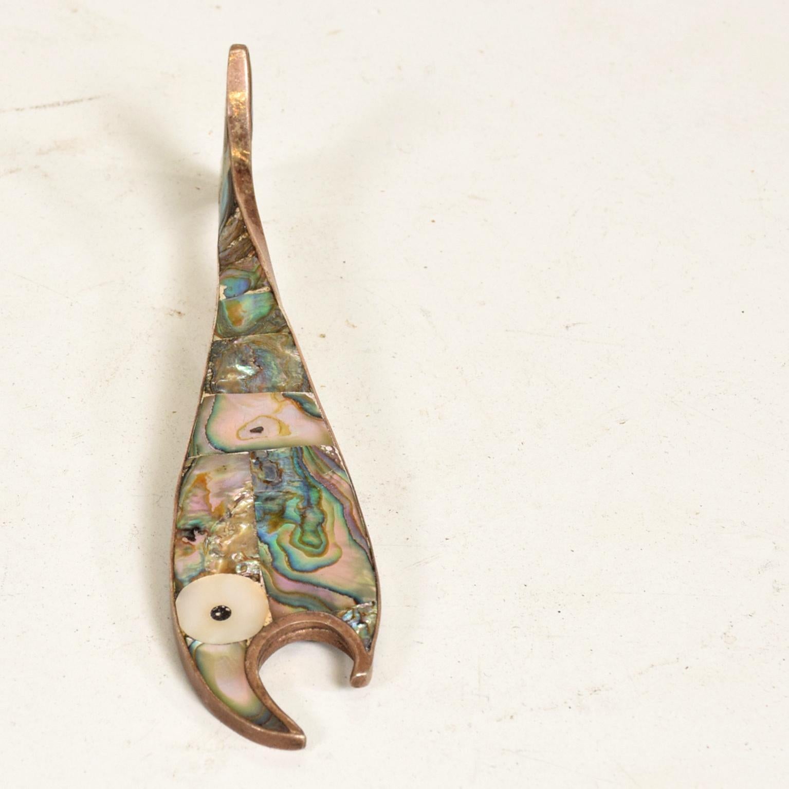 For your consideration, a fish bottle opener abalone. Made in Mexico circa the 1970s. Attributed to Los Castillo. Unmarked.

The bottle opener is a single piece with a twisted fin at the end. Beautiful sculptural shape and nicely decorated with