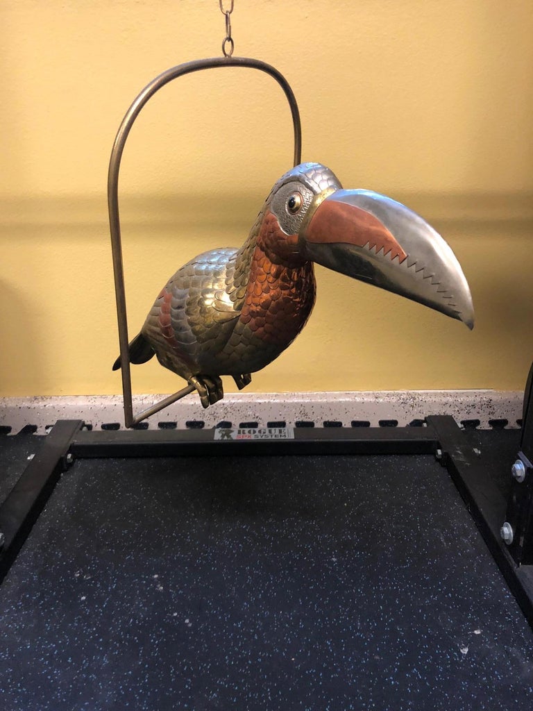 A very large mixed metals (copper, brass and nickel (I believe)) toucan bird sculpture on a hanging perch signed by noted Mexican artist, Sergio Bustamante, circa 1970's. The toucan is approximately 20