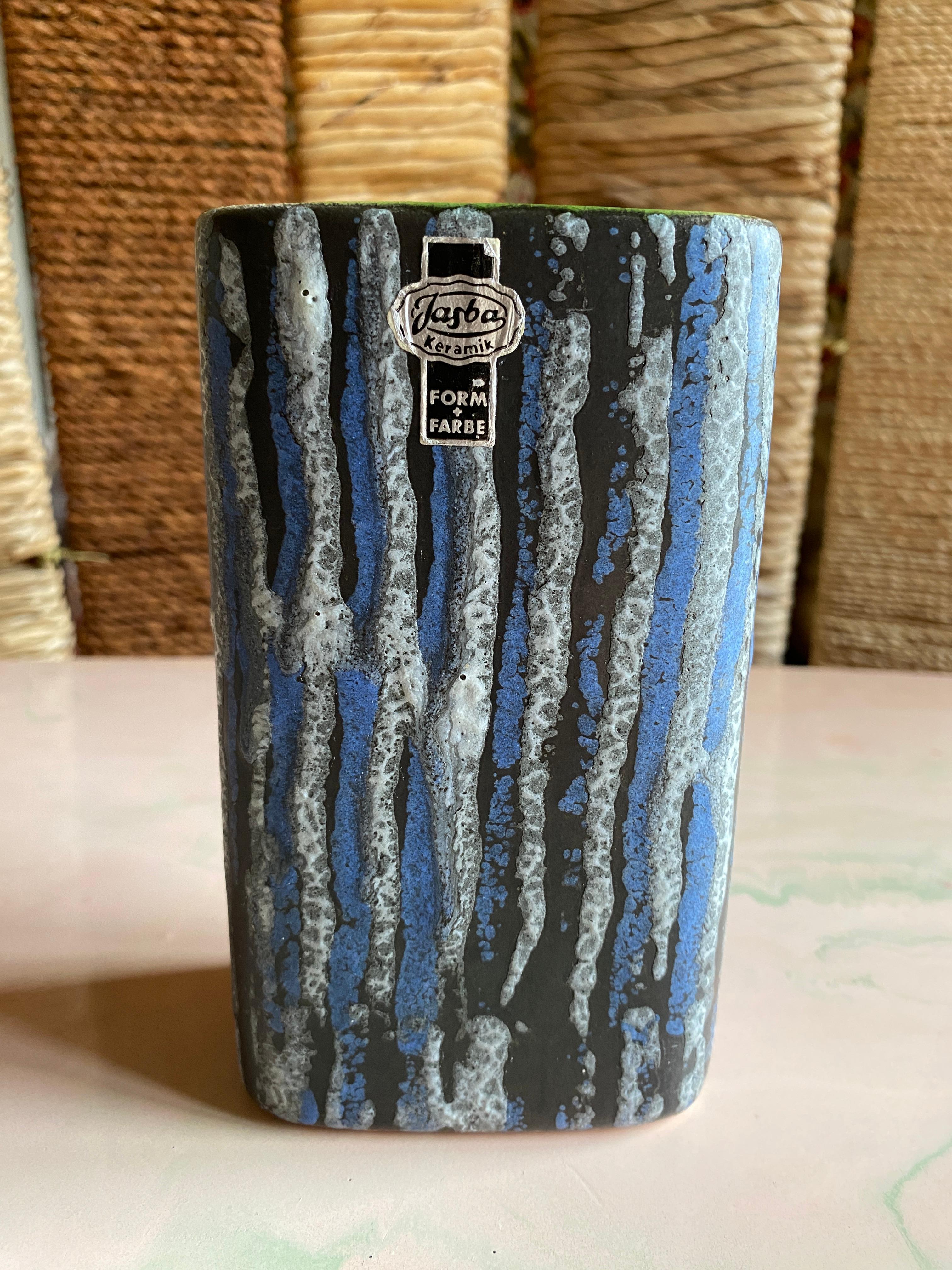 Si tratta di un raro vaso quadrato in gres prodotto da Jasba negli anni '60 in Germania Ovest.  Il vaso presenta un design quadrato unico con quattro angoli arrotondati. È ornato da un fondo nero opaco con strisce di smalto blu pallido e bianco/nero