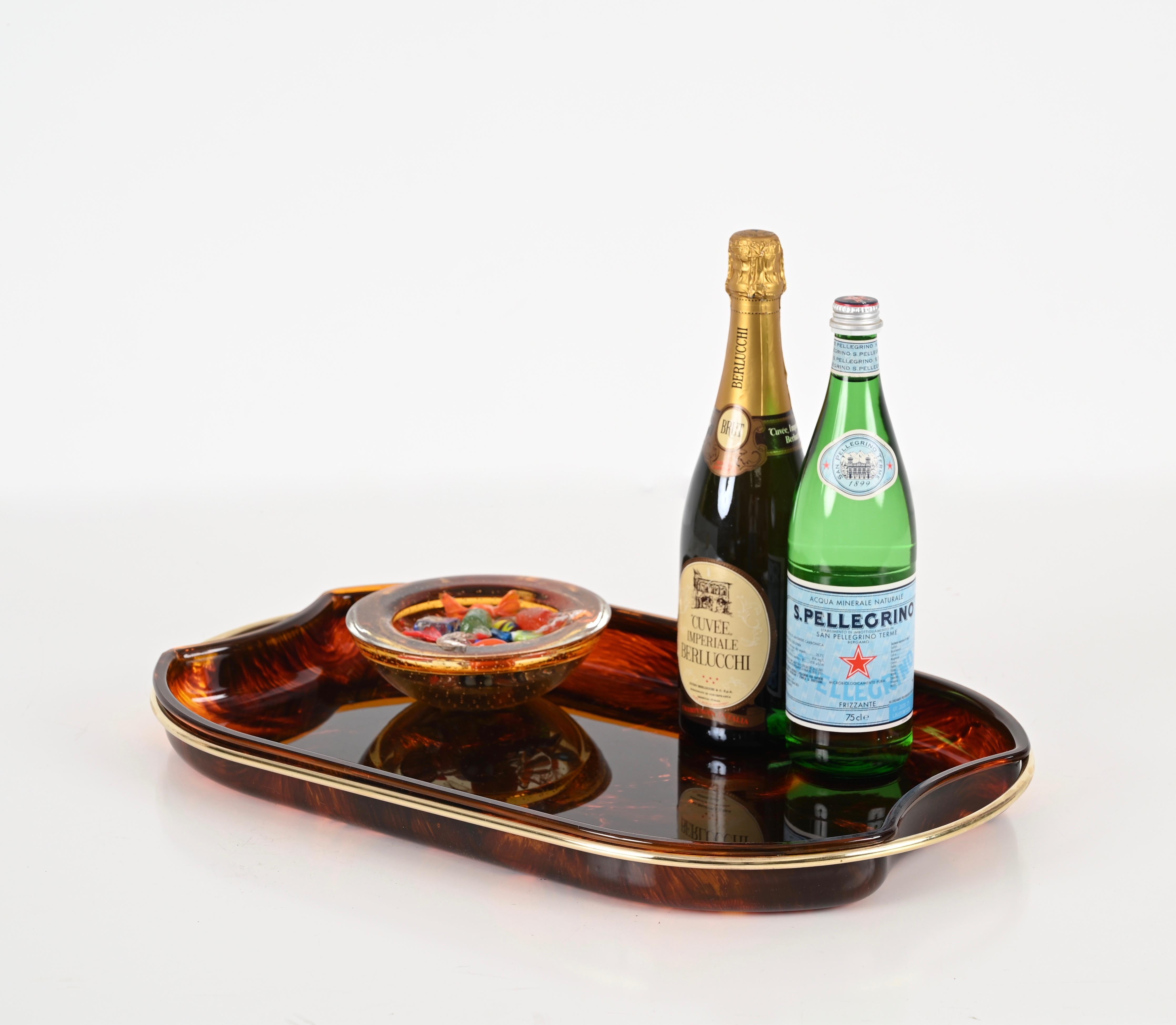 Wonderful and large Mid-Century tray in a gorgeous lucite with a tortoiseshell effect and brass.  This amazing piece was designed in Italy during the 1970s by Guzzini.

This charming serving tray is fantastic thanks to its materials and sinuous