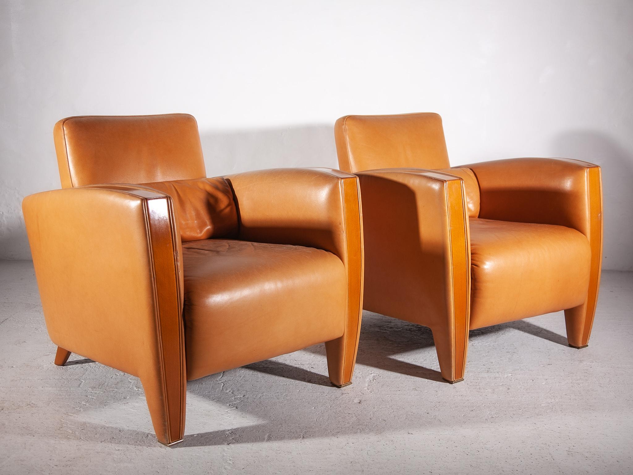 L'ensemble de deux fauteuils club de style moderne du milieu du siècle se caractérise par un magnifique revêtement en cuir camel de qualité chaude avec des accoudoirs en noyer, ce qui ajoute du caractère et de l'authenticité à tout espace de vie.