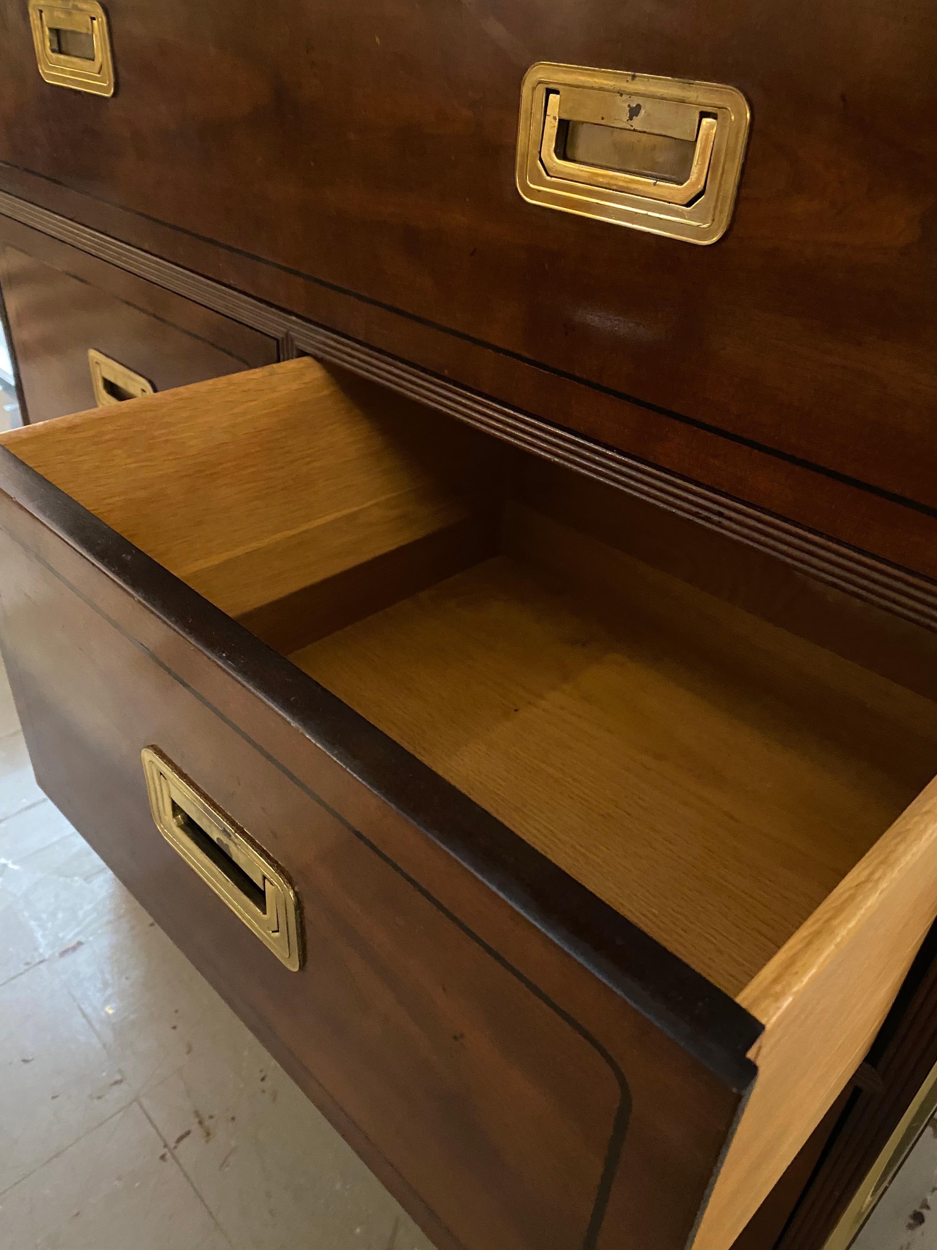 This tall Campaign-style chest of drawers by Baker is crafted from rosewood, featuring bookmatched veneer that showcases the natural beauty of the wood's grain. The design is enhanced by polished brass mounts and drawer pulls, providing a strong