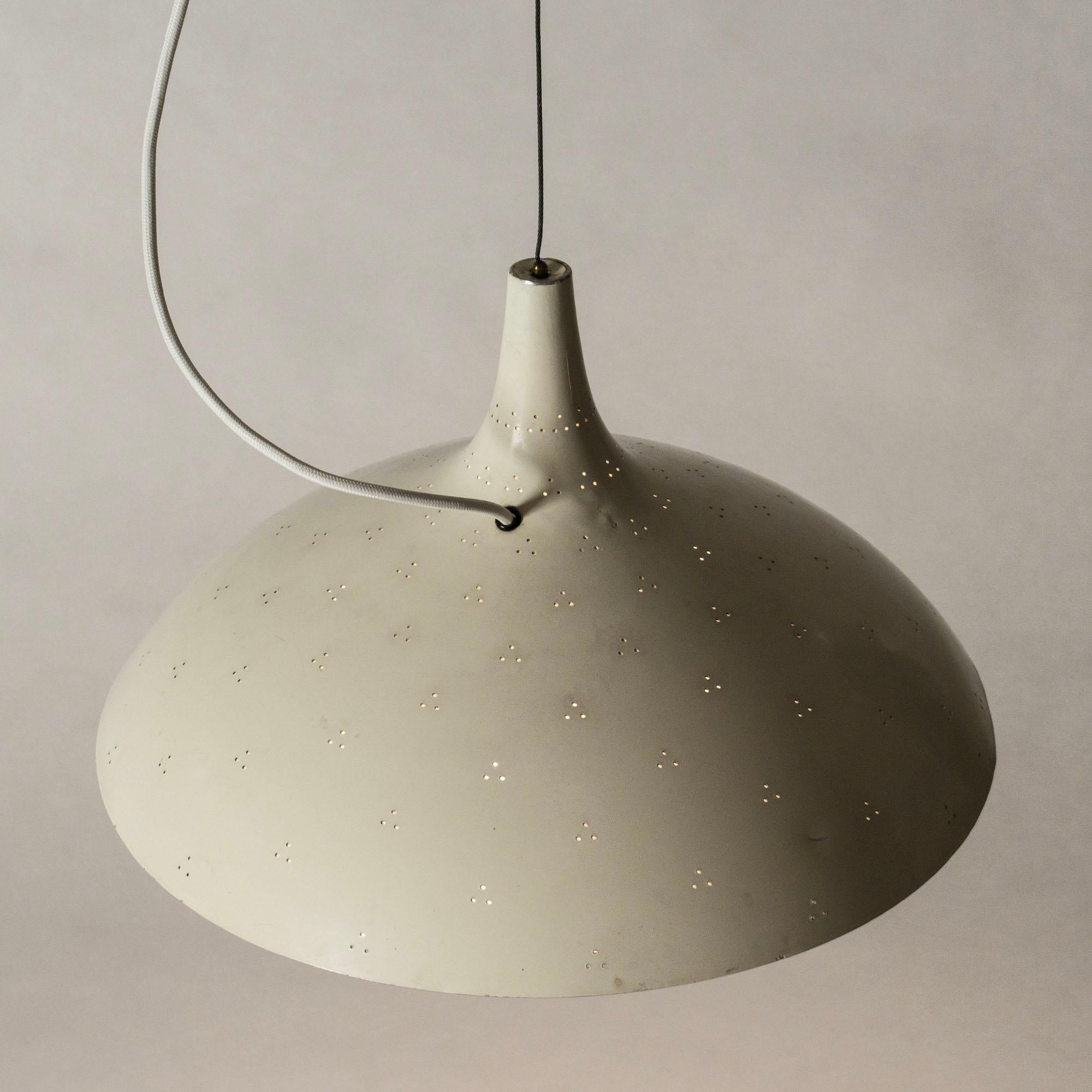 Elegant white lacquered brass ceiling lamp by Paavo Tynell, with a streamlined shade perforated with small holes. The underside of the lamp has a glass shade that covers the light source. Suspended with a brass cord, height adjustable with a brass
