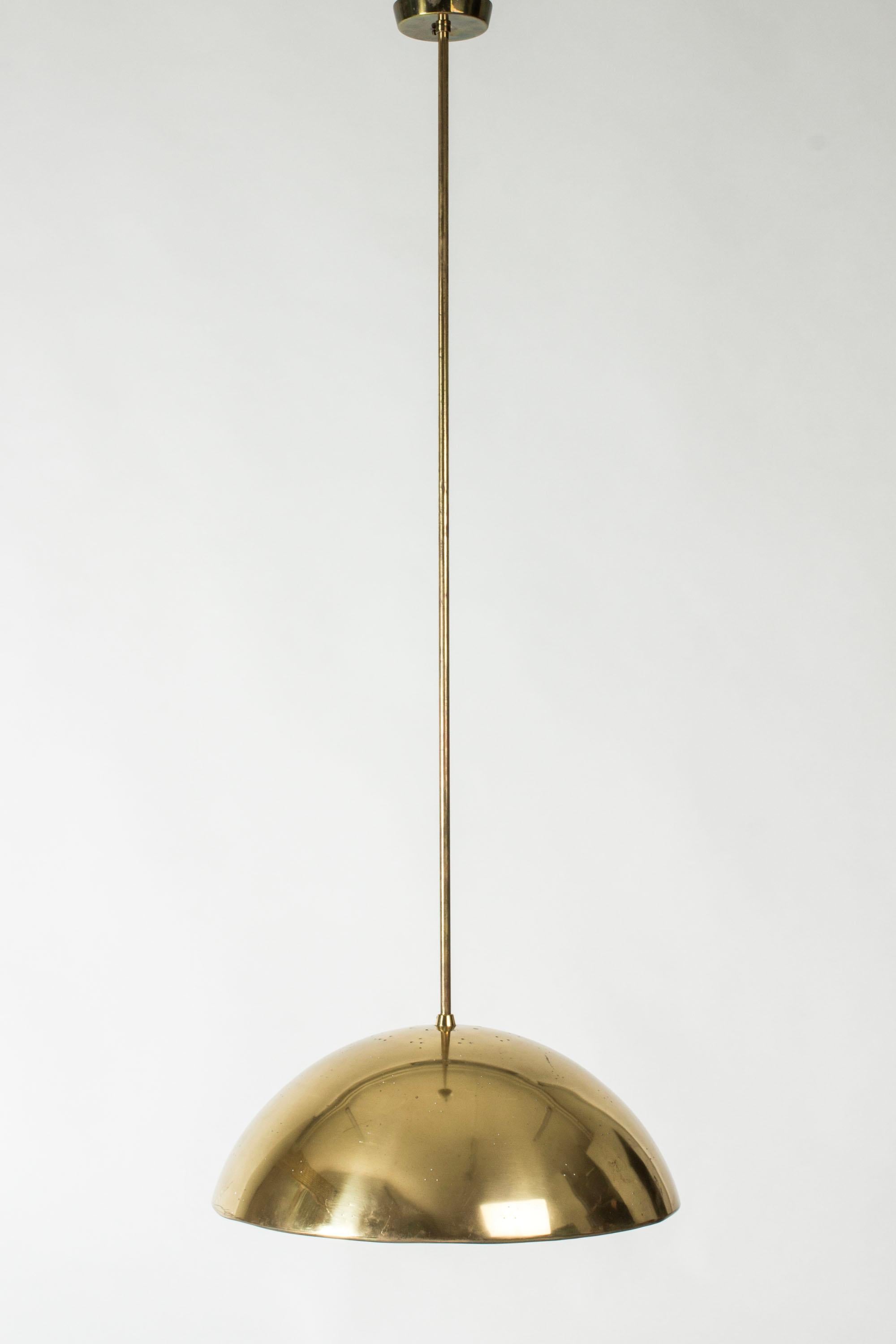 Elegante lámpara de techo de latón de Paavo Tynell, con un largo vástago que se puede personalizar en longitud. Pantalla en forma de cúpula con un patrón de pequeños orificios que dejan salir la luz de forma sutil. Un disco de cristal y un botón