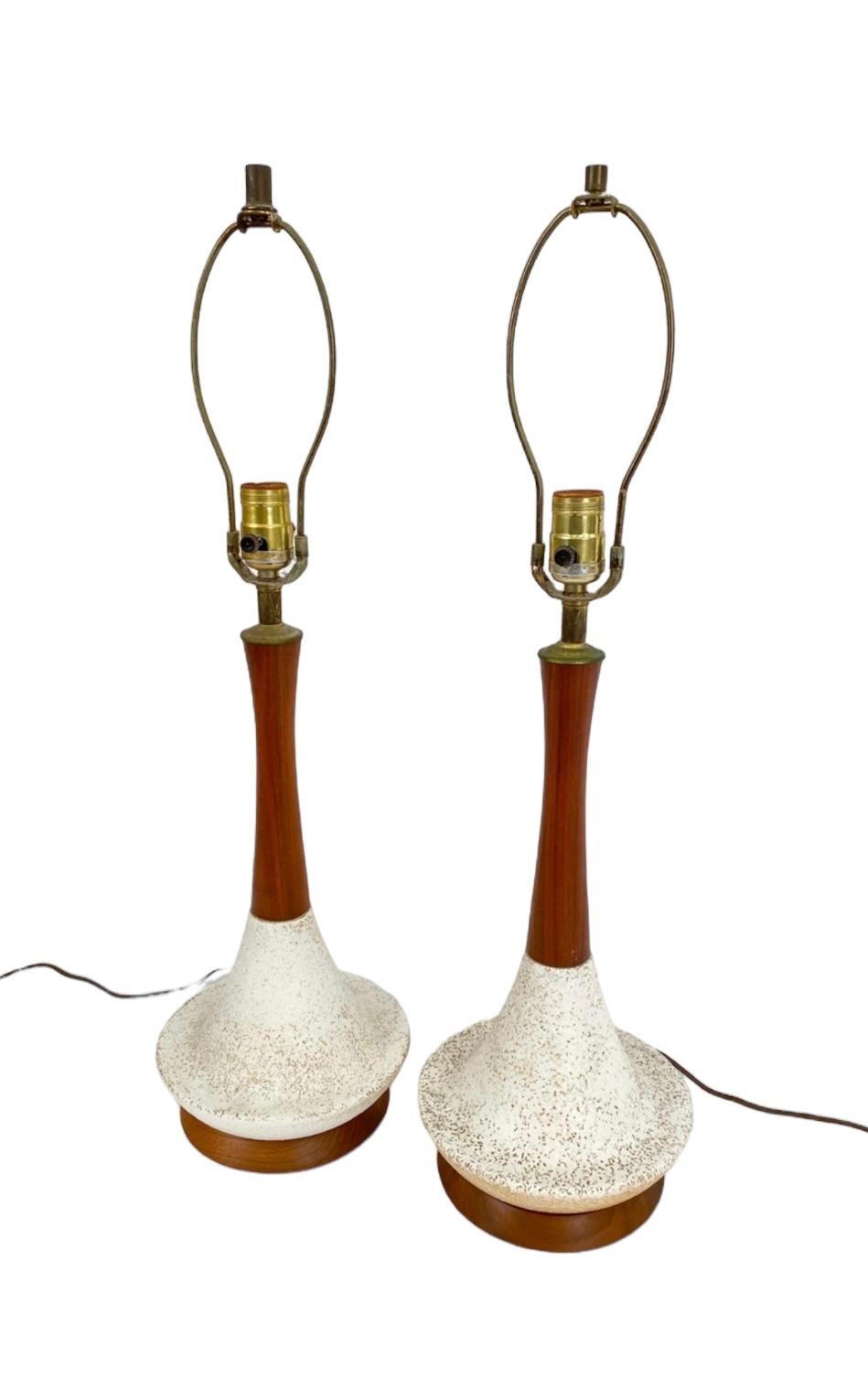 Classic midcentury modern table lamps. Scandinavian style with a combination of elements. Elegant streamlined wooden neck supported by flared speckled ceramic base on wooden disc, accompanied by brass hardware and harp. Wired for US compatibility.