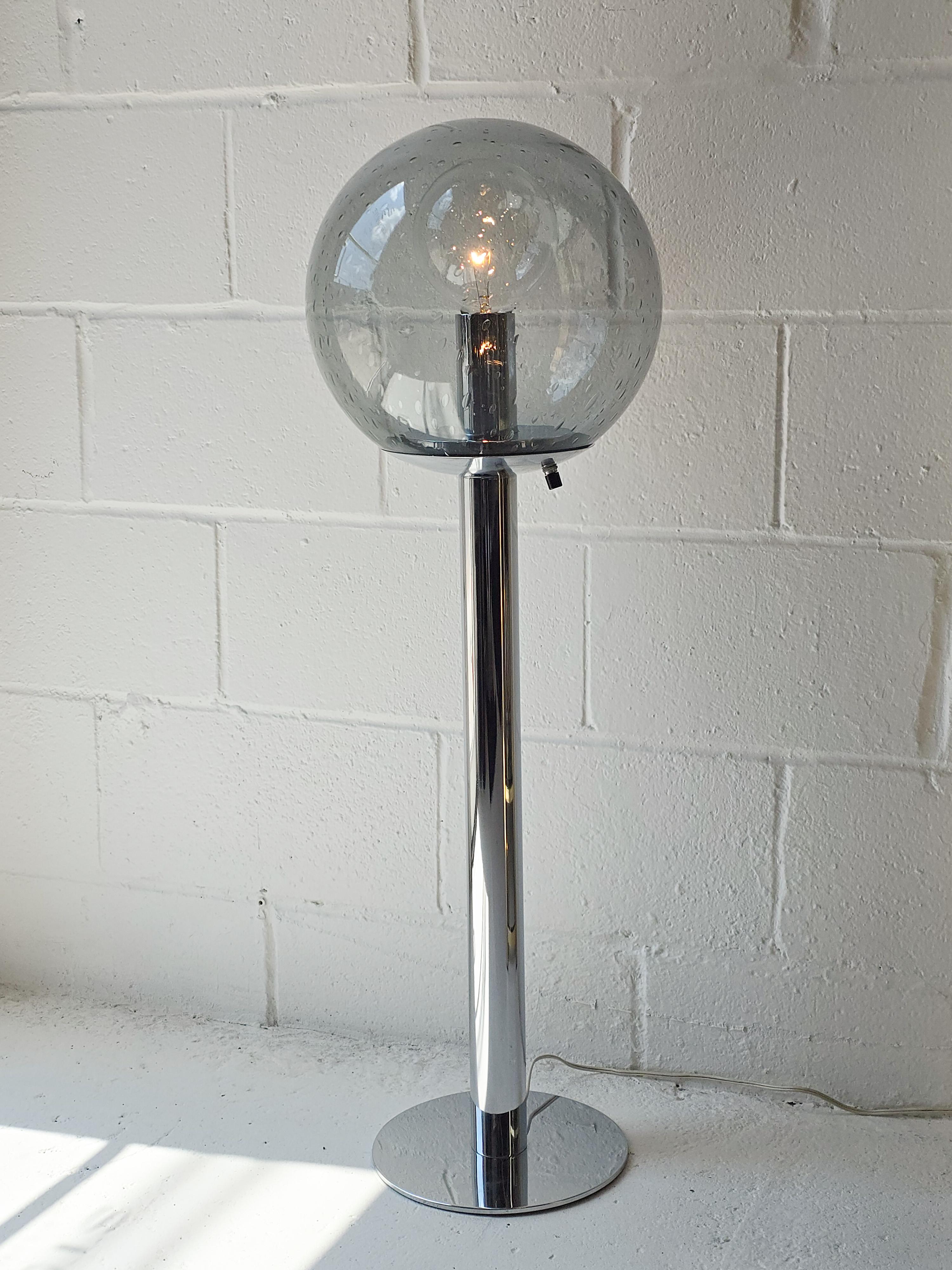 Impresionante lámpara baja de vidrio artístico y cromo tubular. El tamaño de esta lámpara permitía utilizarla como lámpara de pie o de mesa alta. El cuerpo de la lámpara es un tubo cromado, de diseño sencillo pero elegante. La base de la lámpara es