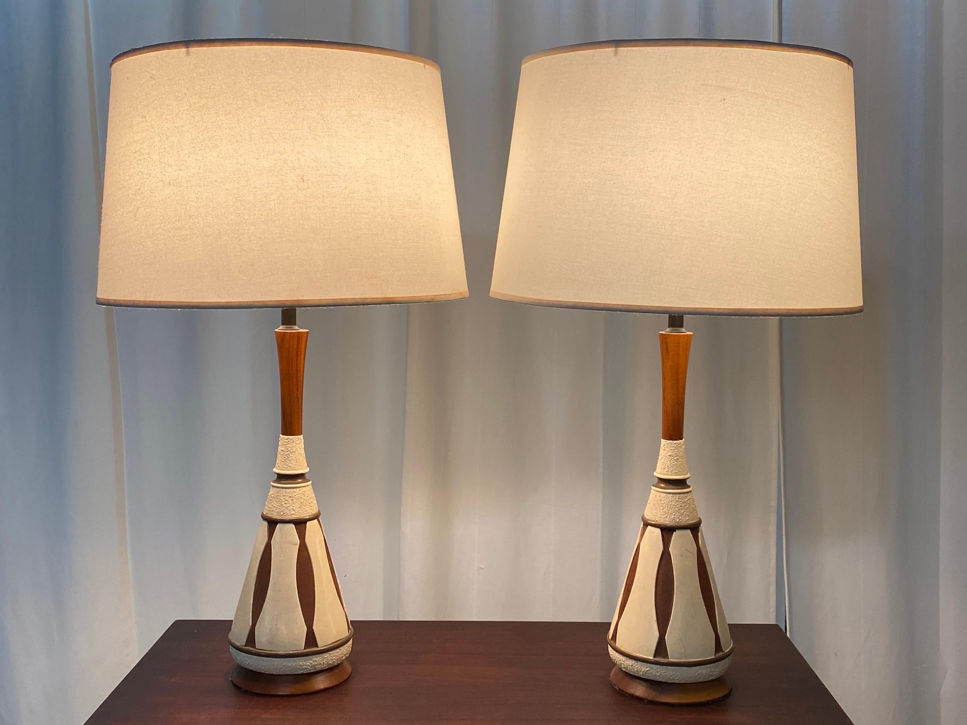 Gorgeous pair of Danish modern ceramic and teak table lamps. Elegant styling and silhouette with warm wood tones. Both work well and feature matching barrel shades and finials. Wonderful lines makes them interesting in their own right yet able to