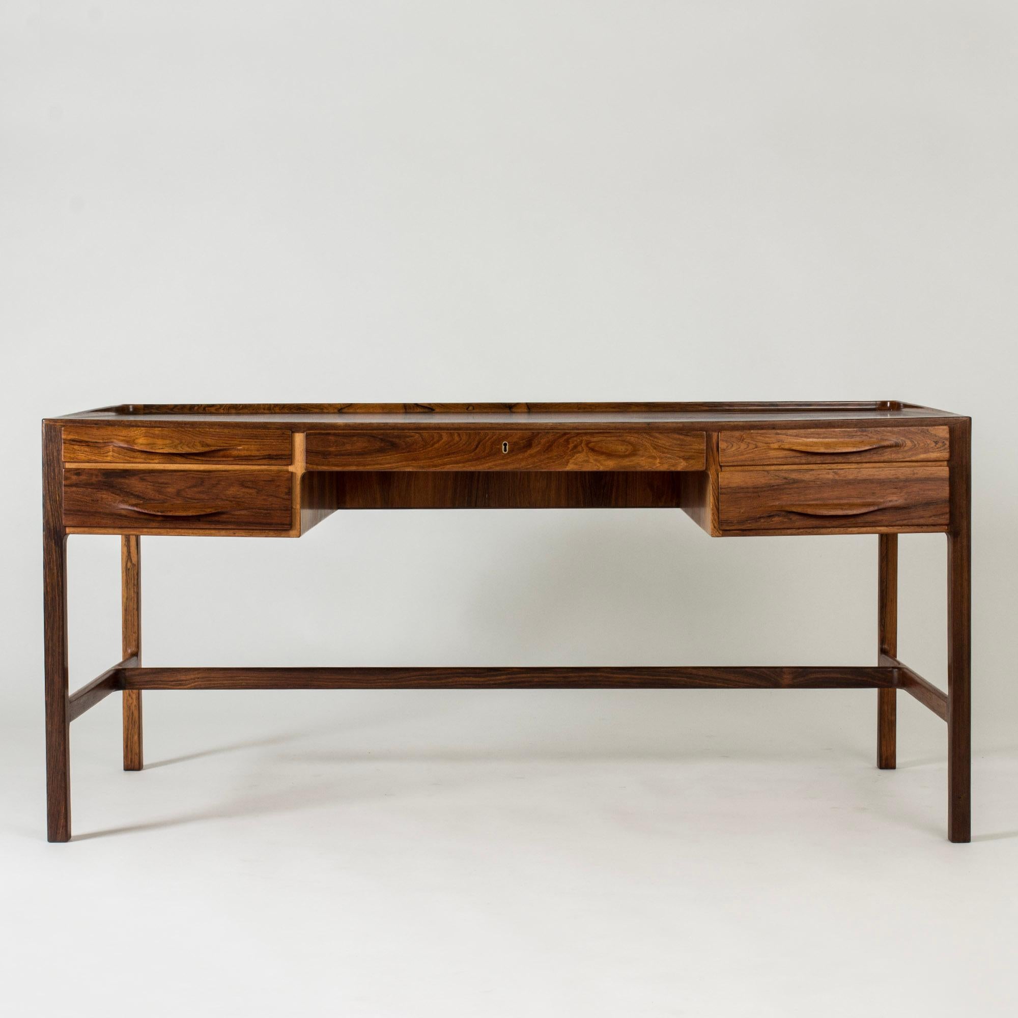 Elegant, freestanding rosewood desk by Kurt Østervig, in a generous size. Beautifully sculpted handle drawers and a rim along the back edge of the table top.