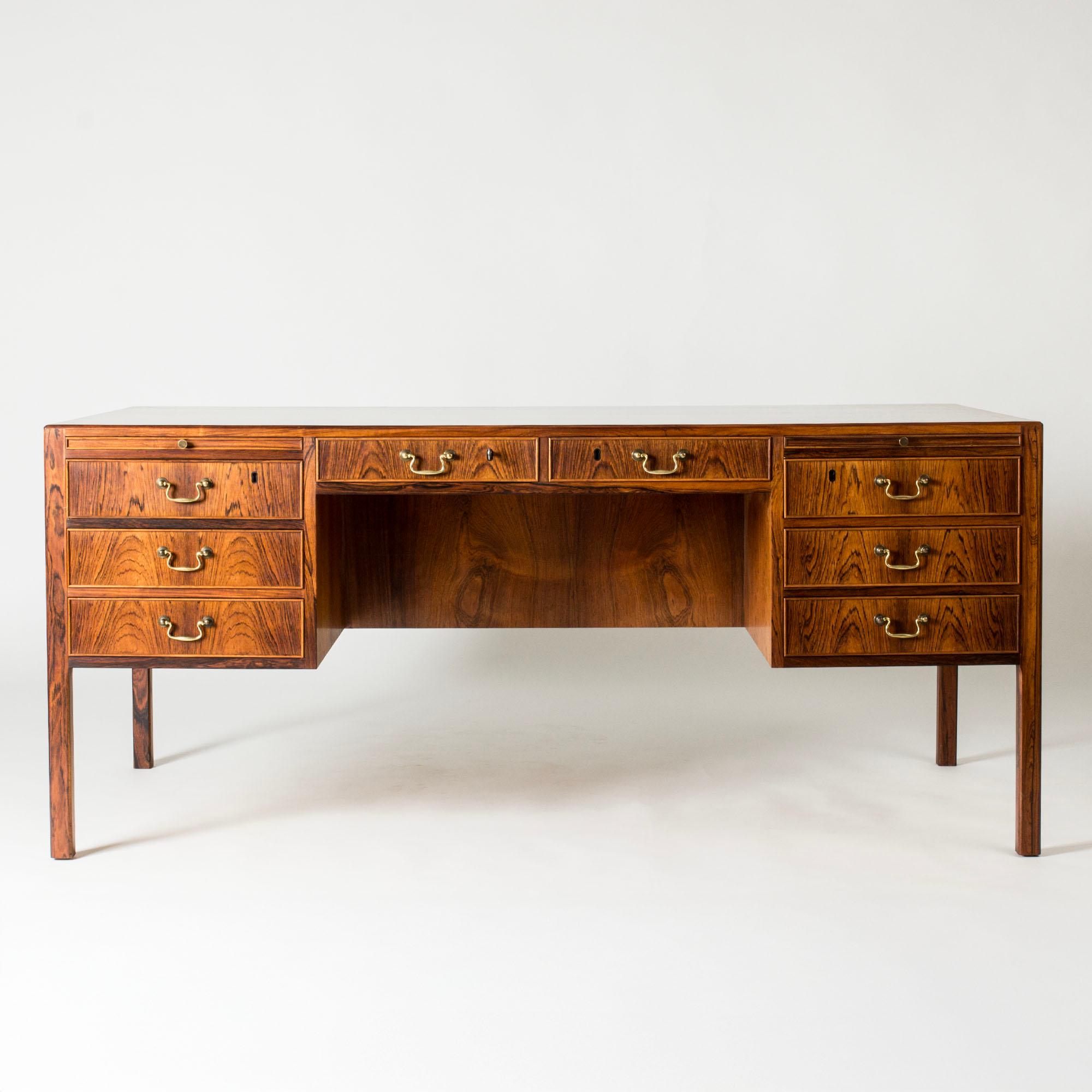 Magnifique bureau d'Ole Wanscher, réalisé en bois de rose aux veinures vives, élégantes poignées en laiton. Des extensions pratiques des deux côtés au-dessus des tiroirs latéraux. Au dos du bureau, il y a deux armoires latérales, des tiroirs et une