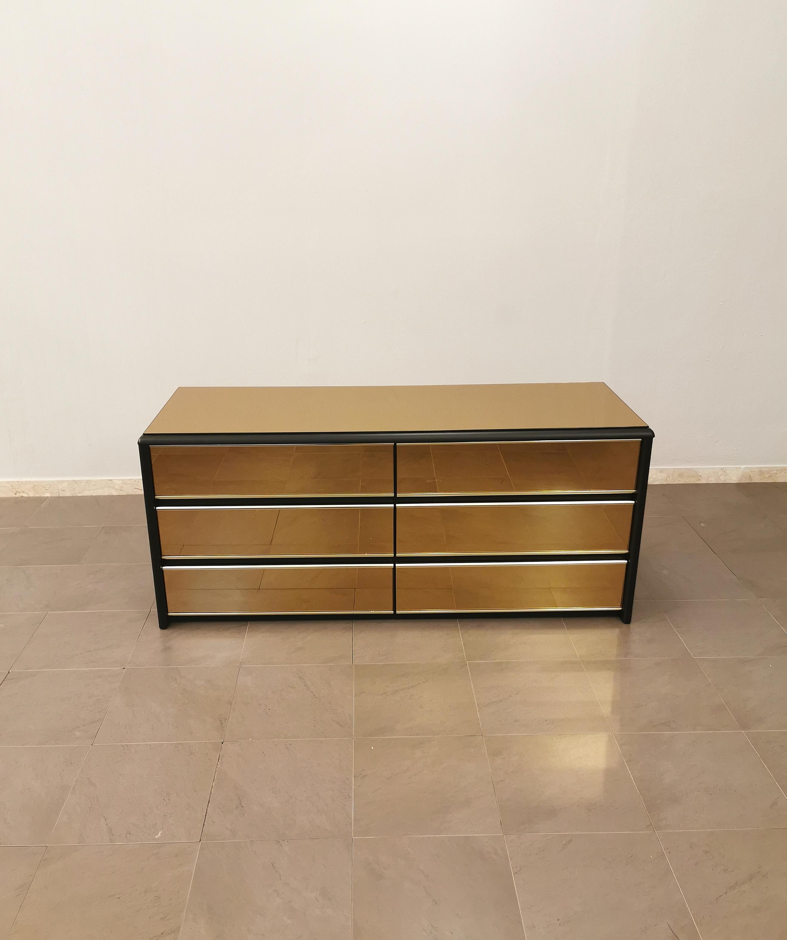 Chest of drawers by an unknown designer produced in Italy in the 70s. This elegant chest of drawers has a matt black wooden structure and rounded edges with top and drawers in caramel-colored mirrored glass and golden aluminum finishes.



Note: We