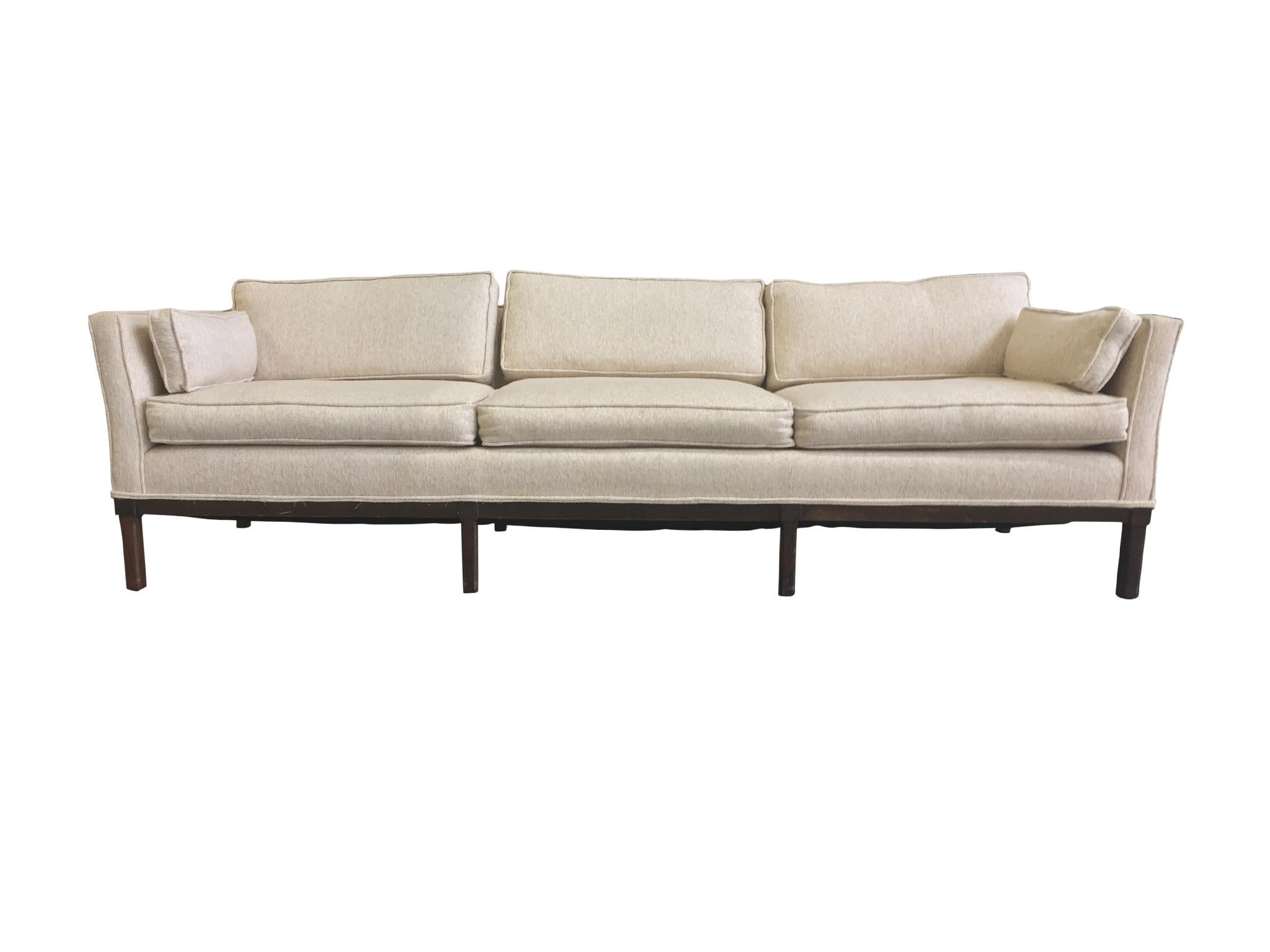 A set comprised of a three-seat sofa and a settee, in the Mid-Century Modern styles of designers such as Edward Wormley. They are upholstered in an off-white, ecru mix of cashmere and wool, and have removable back and seat cushions. The legs and