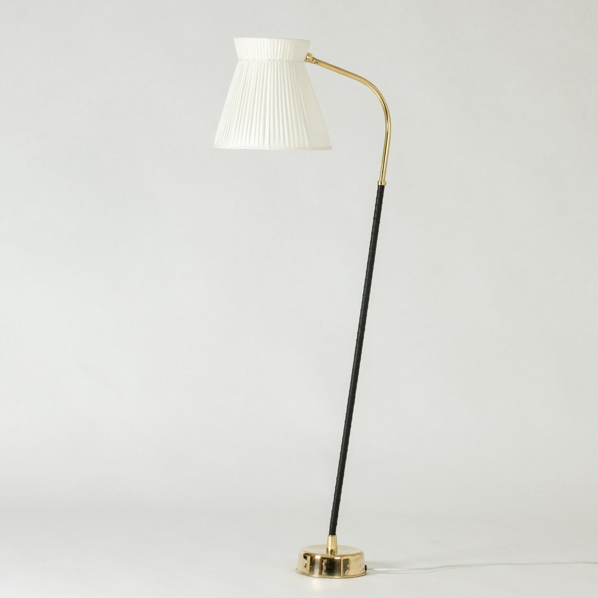 Striking floor lamp by Lisa Johansson-Pape, in a very cool, casually tilted design. Made from brass with stem wound with black leather, voluminous pleated shade.