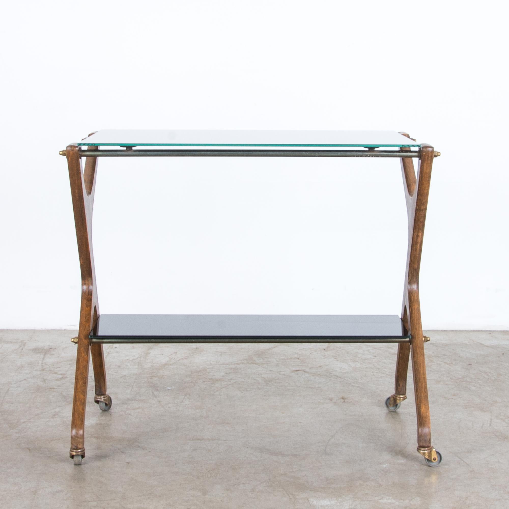 From France circa 1960, a timeless bar cart in hardwood, brass, and glass. High quality materials are elegantly arranged with a Modernist flair. Brass hardware is stylish and practical, giving a sturdy support and precise movement, supporting a