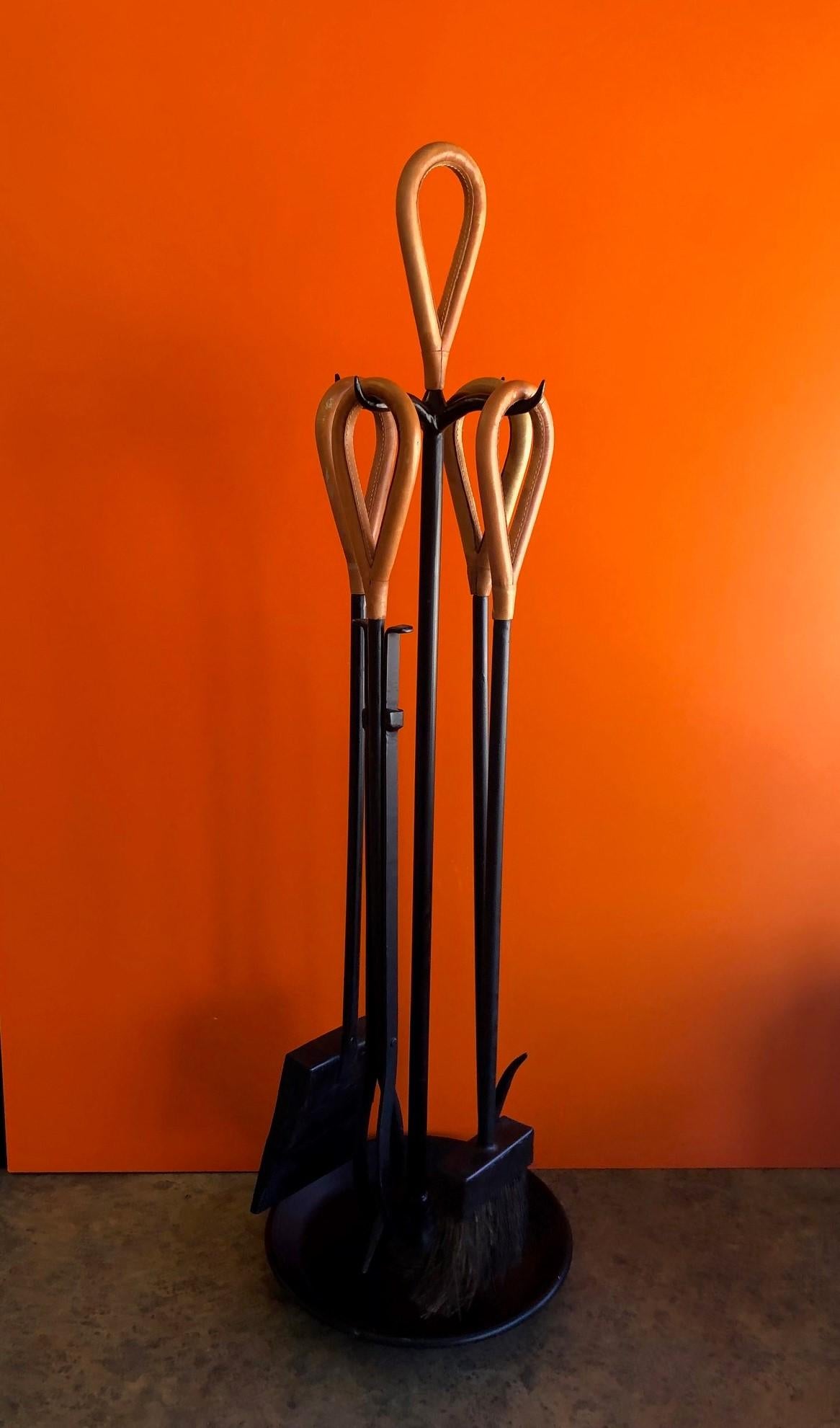 A very cool MCM fireplace tools set in the style of Jacques Adnet, circa 1960s. There are four tools (broom, dustpan, tongs, fire poker) with saddle leather wrapped handles supported by an integral freestanding rack in iron with removable leather