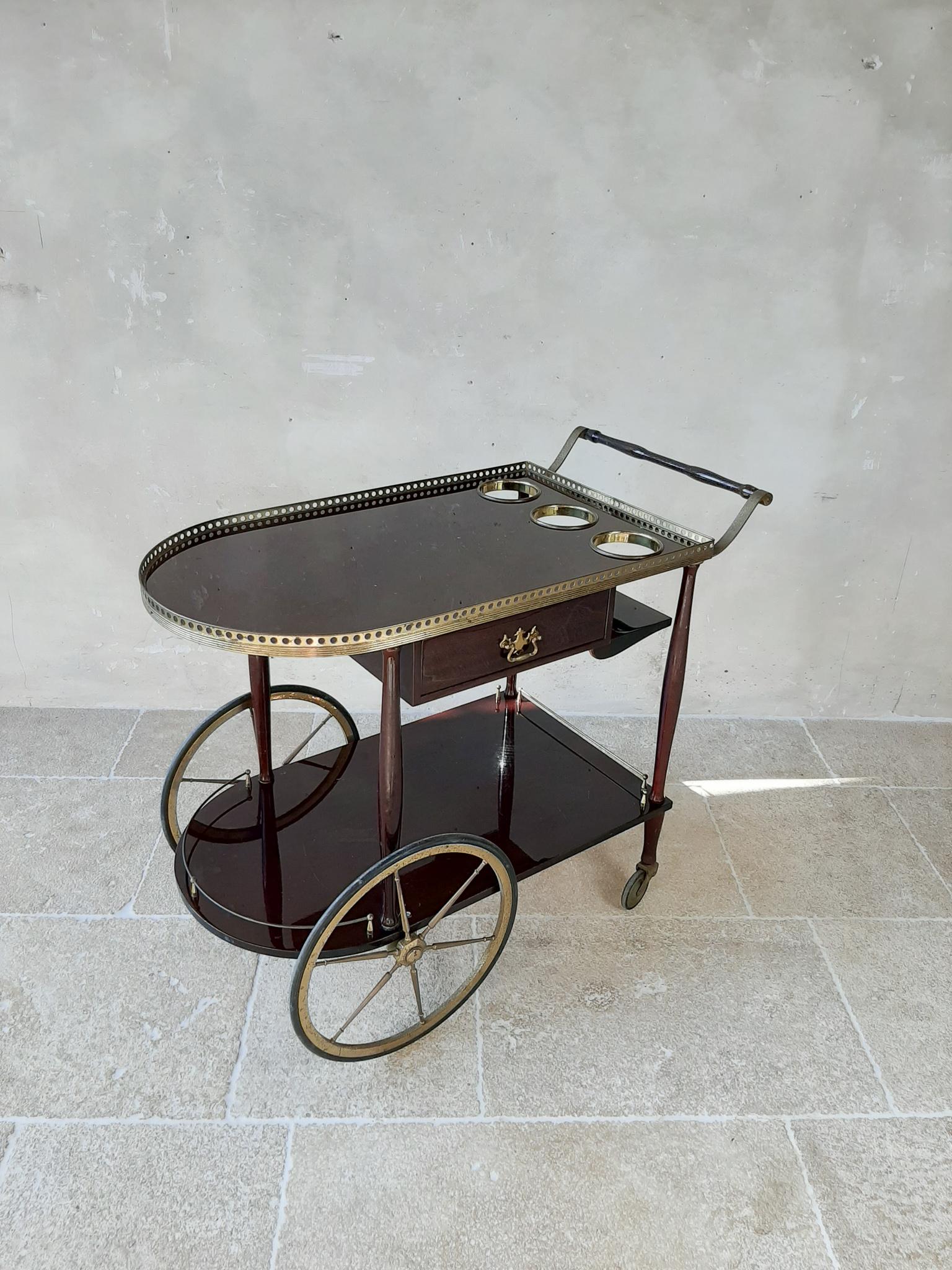Mid-Century Modern Italian mahogany and brass serving trolley in the style of Cesare Lacca and Aldo Tura. This stylish bar cart has a mahogany frame and shelves finished with brass details around the rims, handles and the wheels. This piece has two