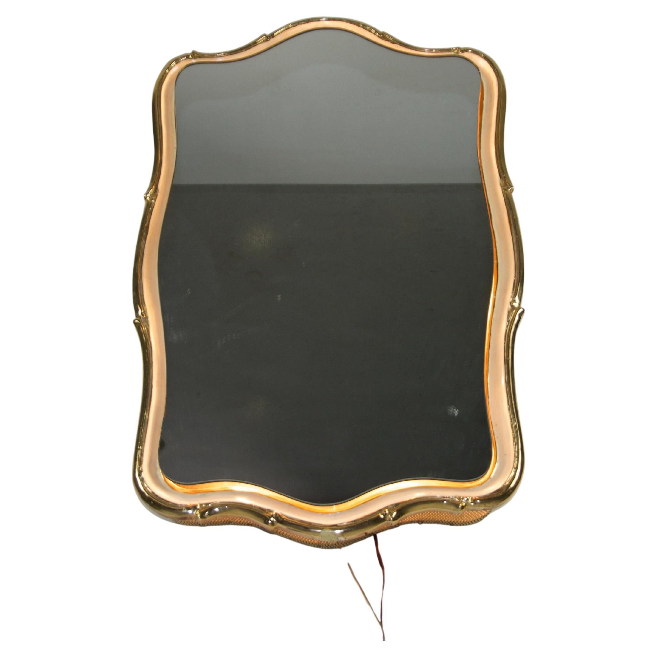 Ce miroir mural en laiton éclairé, datant des années 1960, est un exemple étonnant de l'élégance du design italien. Le miroir est encadré par une belle bordure en laiton aux courbes douces et aux détails subtils, ce qui lui confère une présence