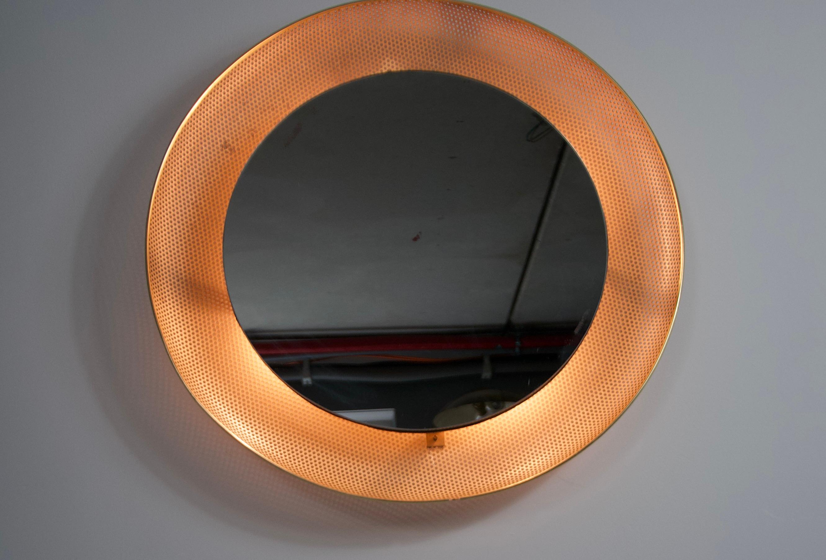 A beautifully crafted round illuminated wall mirror from the 1960s, made in Italy. This midcentury modern piece features a circular brass frame that radiates timeless elegance. The integrated lighting softly highlights the mirror's perimeter,
