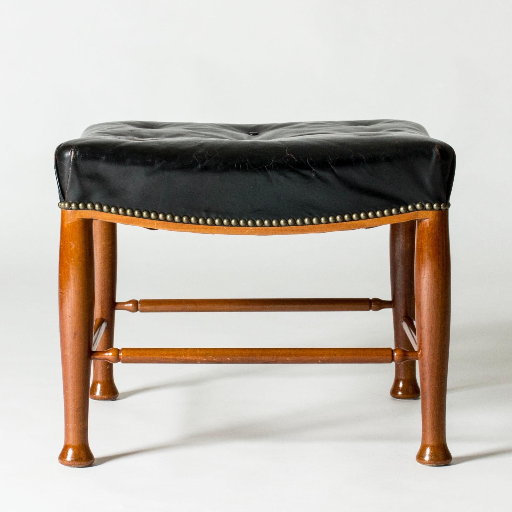 Pouf de Josef Franks, en acajou, avec des pieds élégamment sculptés. Revêtement d'origine en cuir noir patiné, clous décoratifs en laiton sur le bord de l'assise.