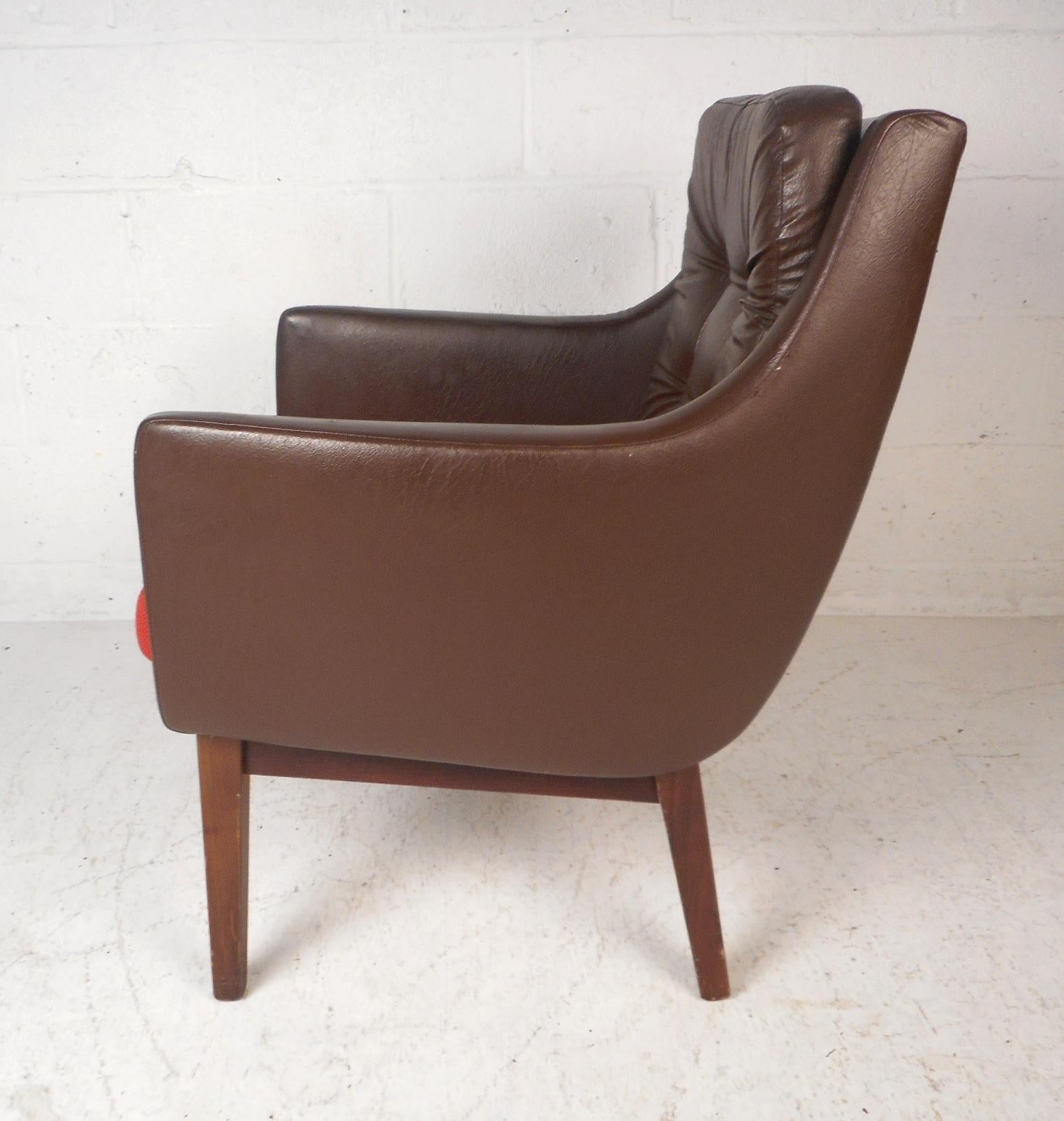 This beautiful vintage modern lounge chair features sloped sides and an angled back rest. This sleek arm chair ensures maximum comfort without sacrificing style. An overstuffed removable cushion, angled legs, and a tufted back rest add to the