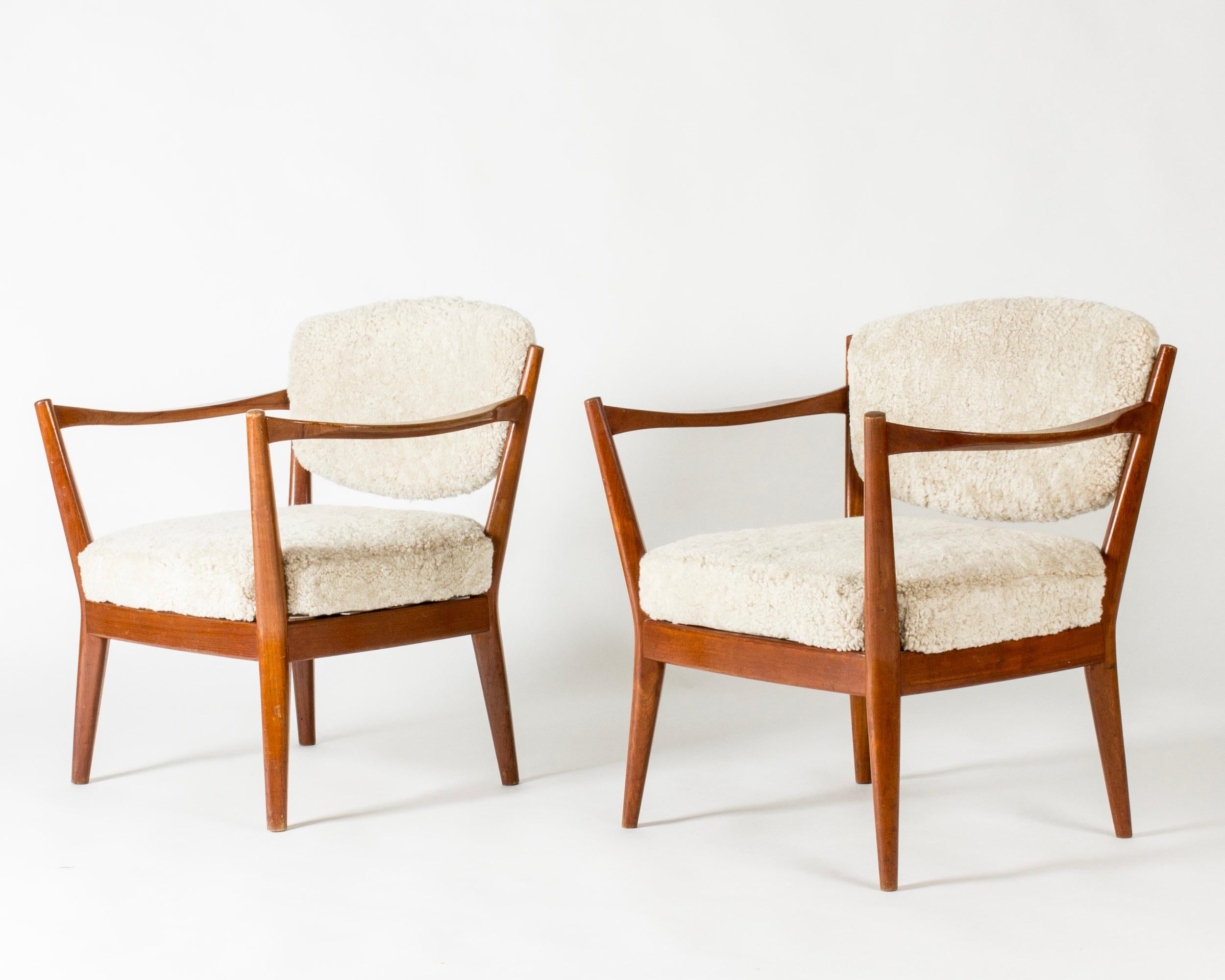 Pair of elegant fire place chairs by Fredrik Kayser, with teak frames, beautifully sculpted. Neat size. Backs and seats upholstered with offwhite sheepskin.