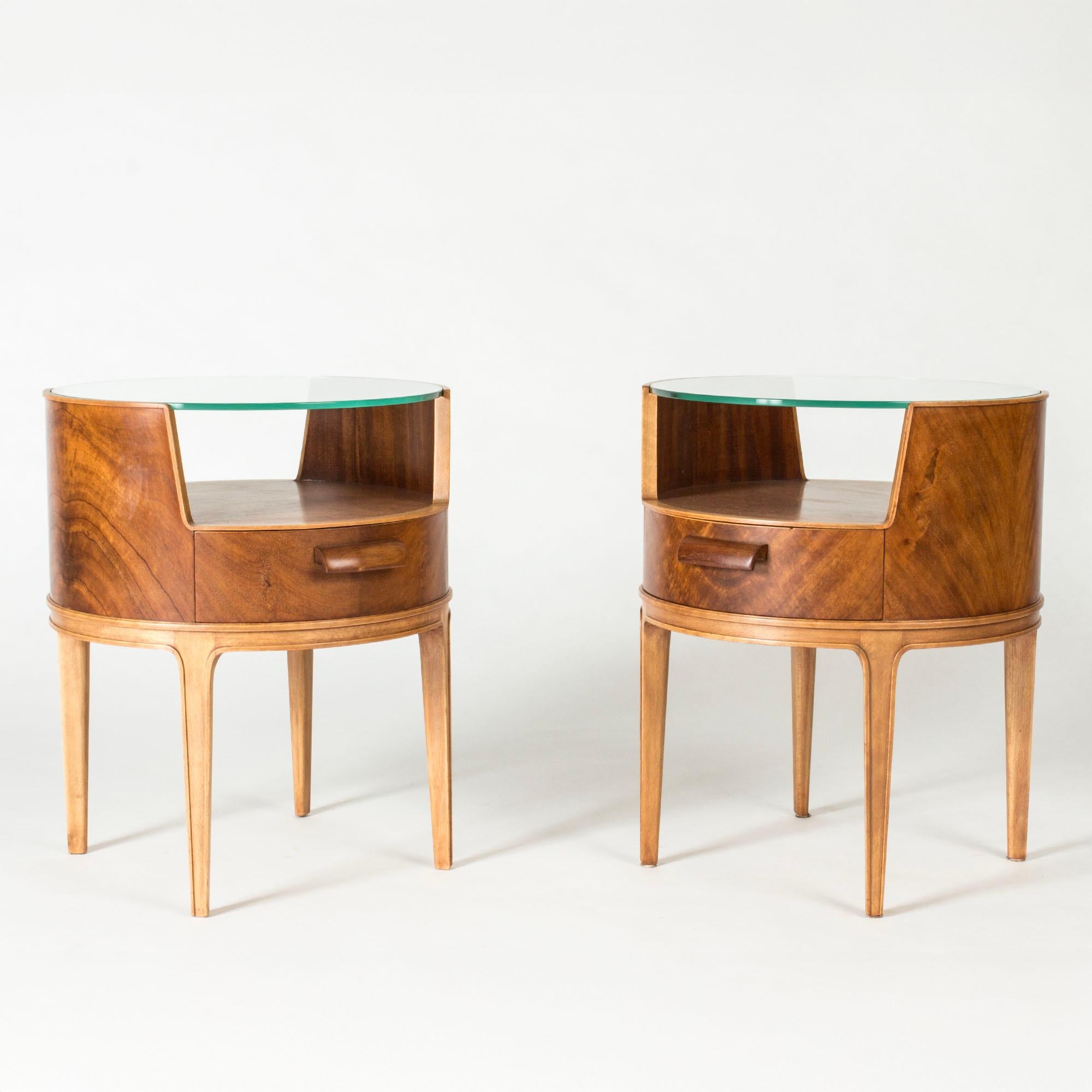 Pair of beautiful bedside tables by Axel Larsson, with mahogany veneer, glass tops and sculpted wooden handles.