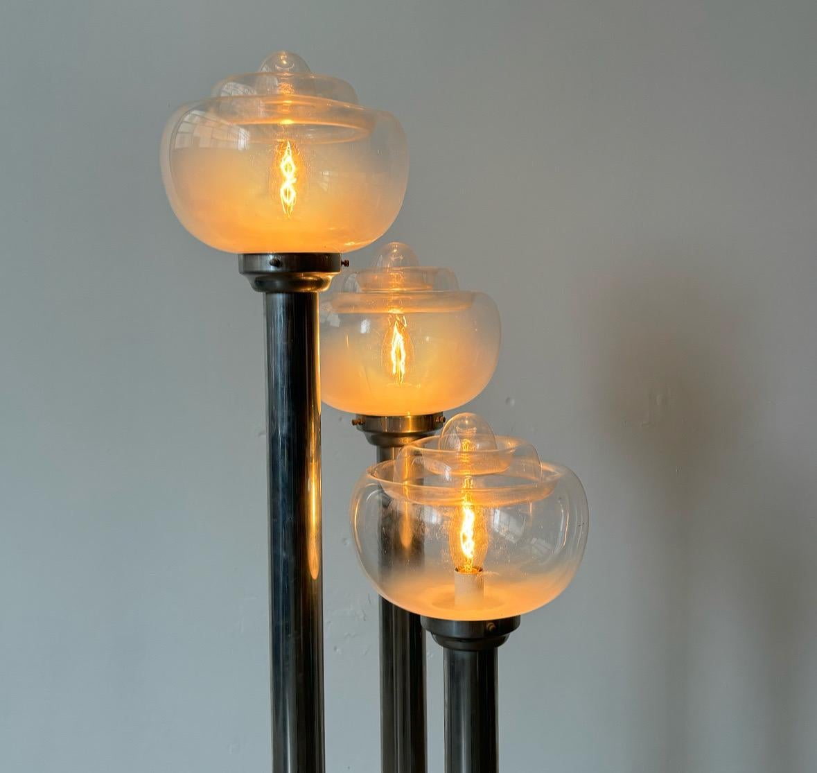 Diese atemberaubende Stehlampe aus verchromtem Stahl aus den späten 1960er bis frühen 1970er Jahren verfügt über drei mundgeblasene Murano-Glasschirme, die von Mazzega hergestellt wurden. Jeder Schirm geht nahtlos von klarem zu opalisierendem Glas