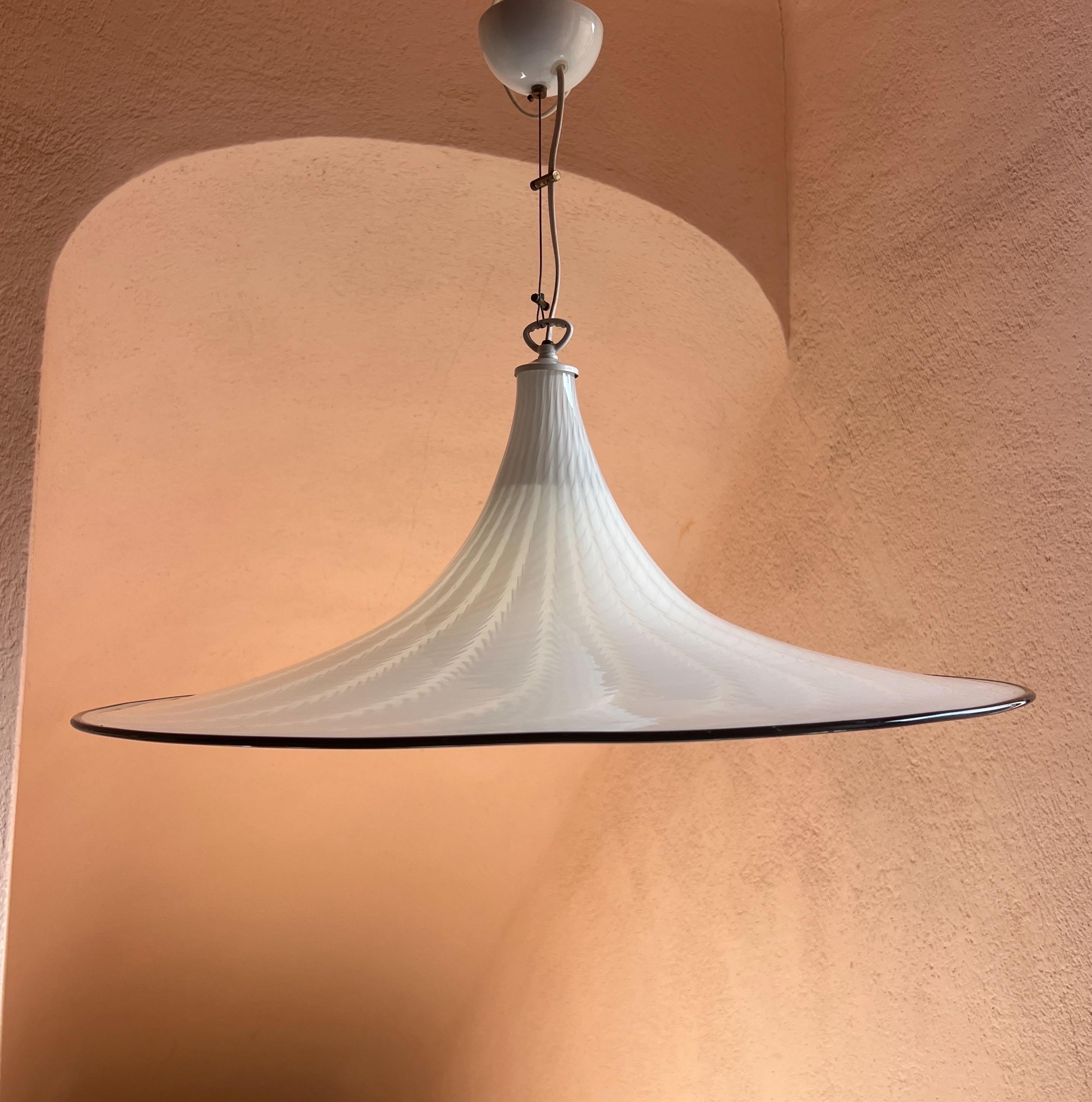 Questa eccezionale lampada a sospensione degli anni '70 è un esempio straordinario di design italiano di metà secolo. Il vetro di Murano soffiato a mano ha l'elegante forma di un cappello a tesa larga, che conferisce al pezzo una raffinata presenza