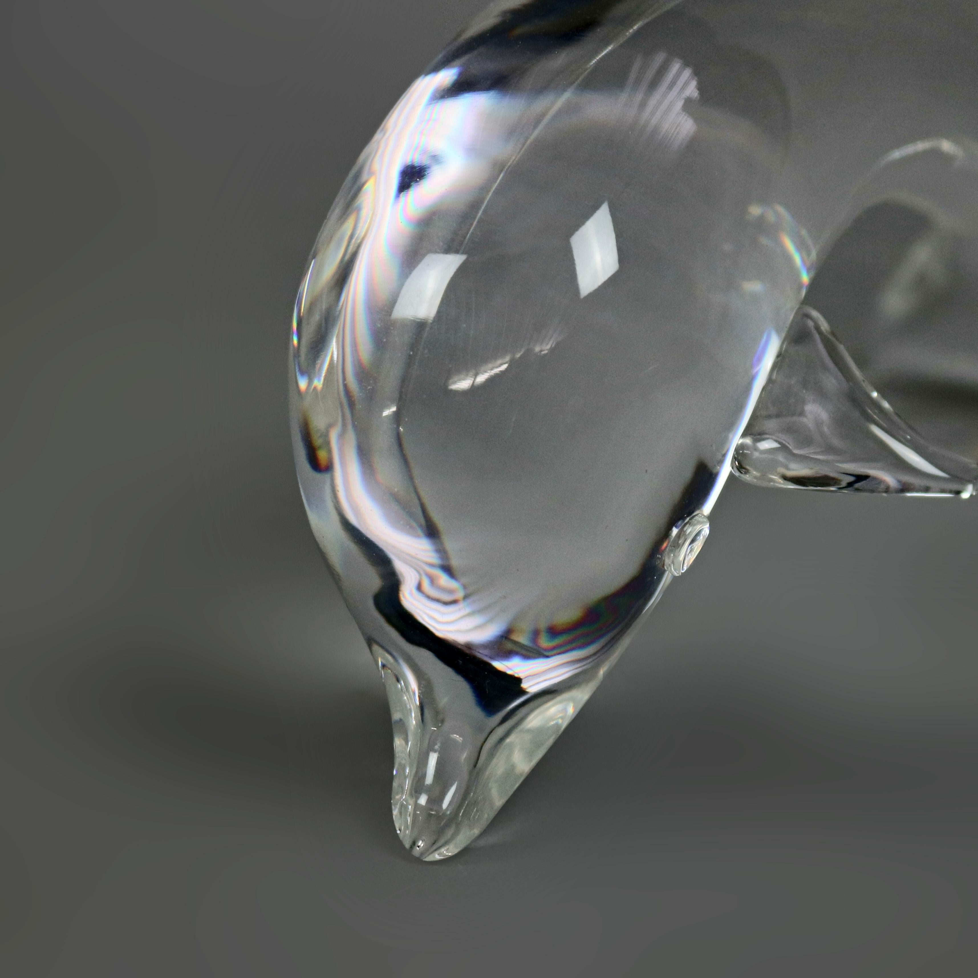 A Midcentury Modern Steuben figurative mouth blown crystal sculptural paperweight features colorless art glass in full body form of a swimming dolphin, designed by Lloyd Atkins, 1960 for Corning Museum of Glass, New York, NY, unsigned, 20th